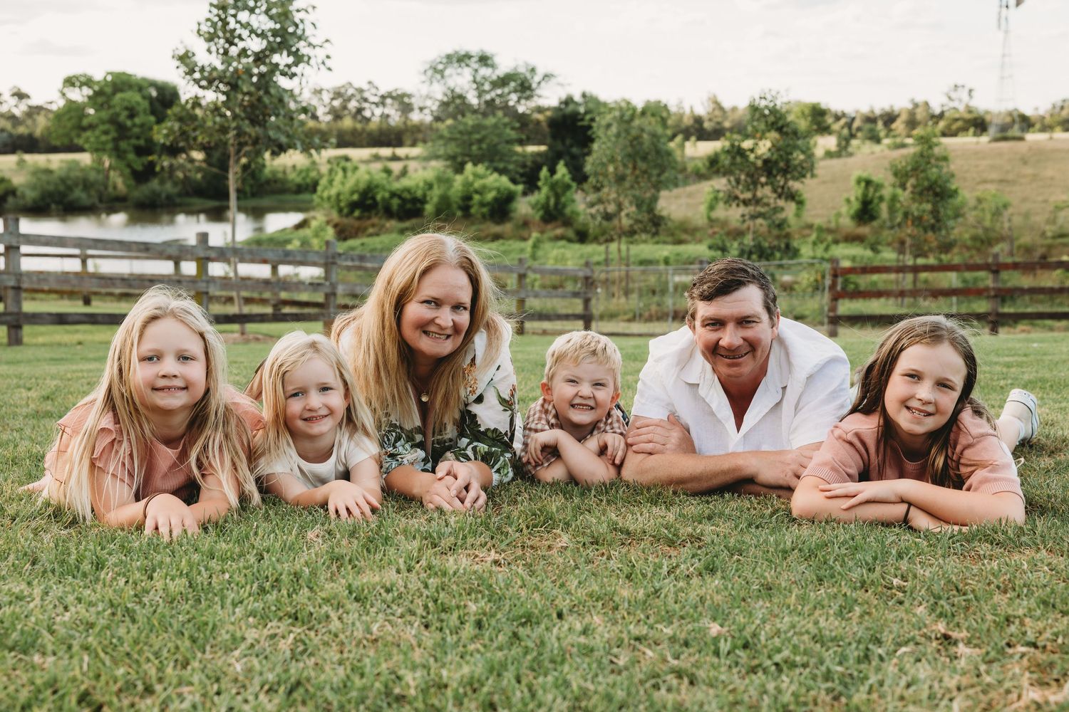 Happy family of six lying on green grass smiling at camera on a sunny day outdoors.