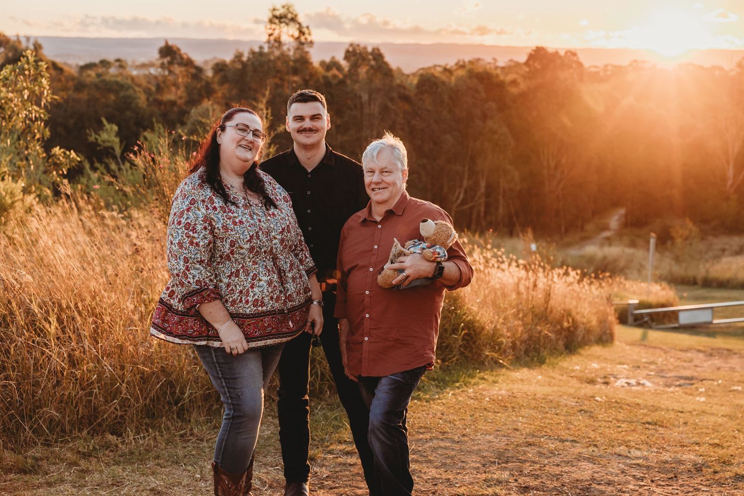 Three generations family portrait at golden sunset in open field.