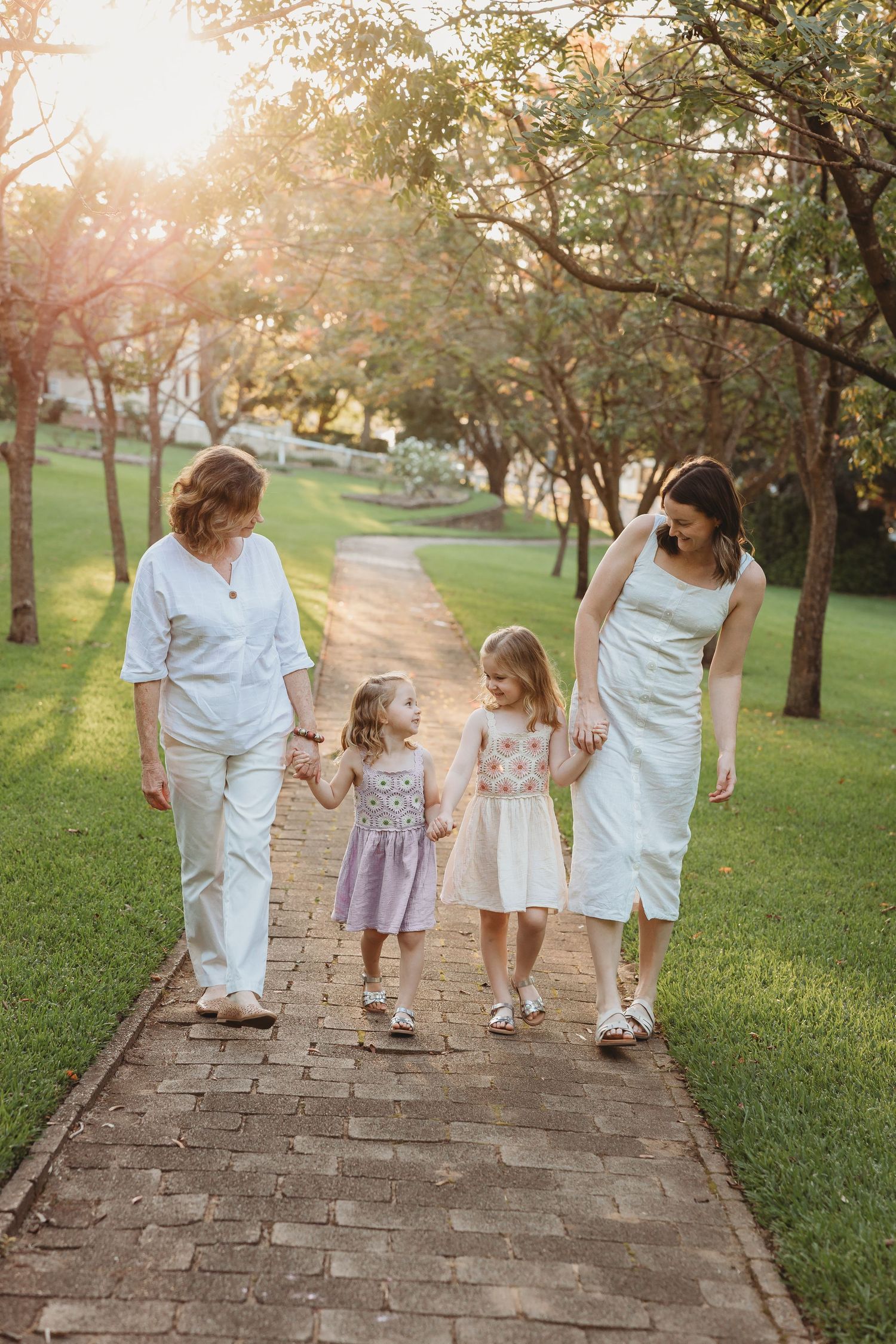 Grandmother and mother walking with two young girls on a sunny park path.