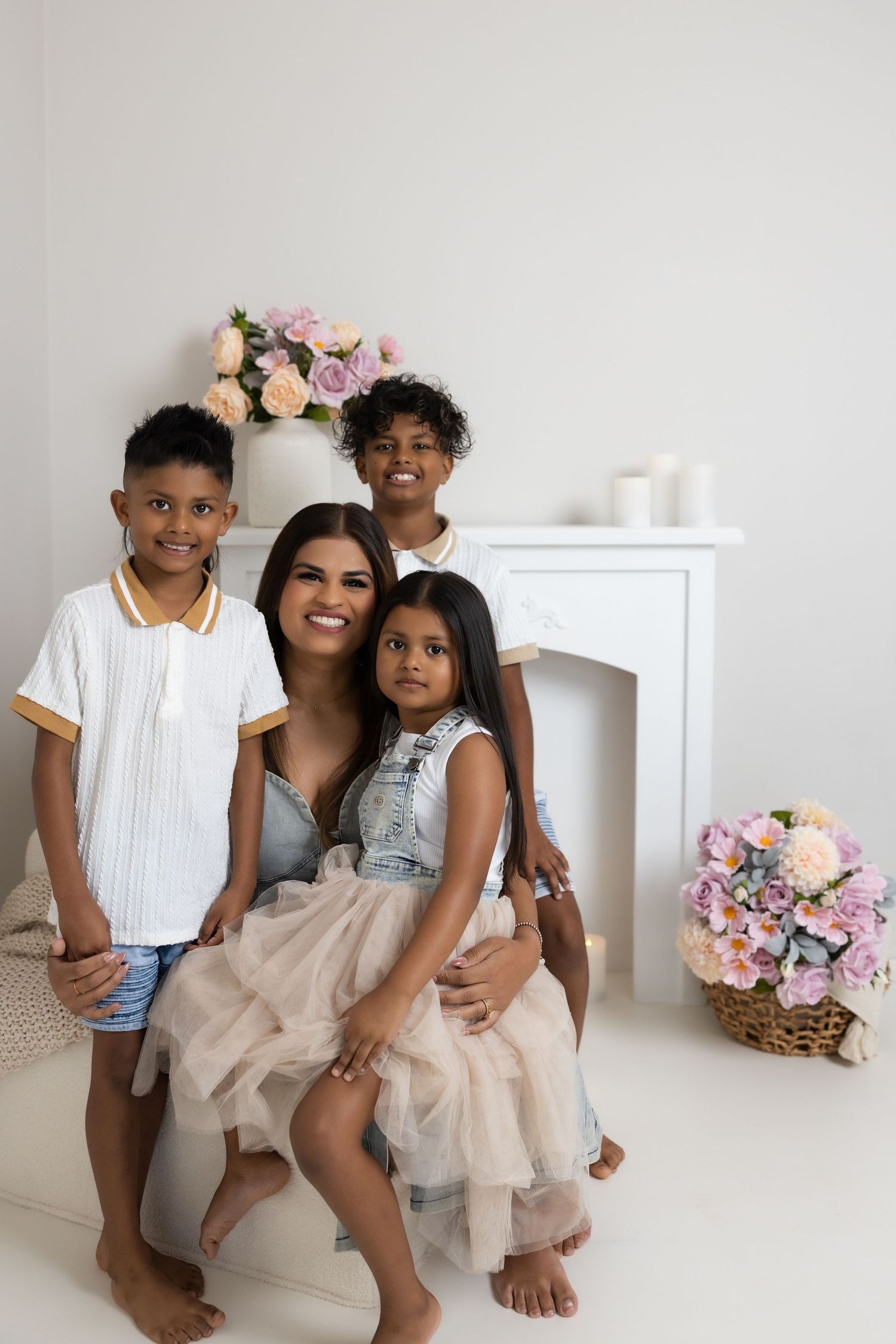 Smiling mother with three children posing indoors near white fireplace with floral decorations.