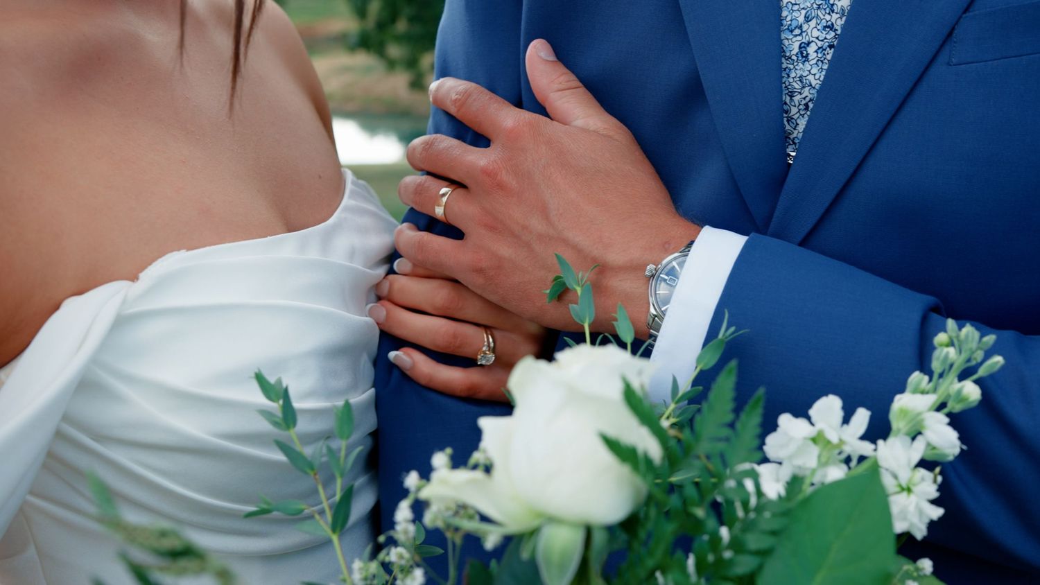 Close-up of wedding rings and hands against formal wedding attire.