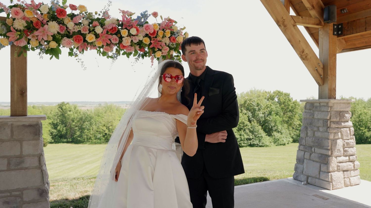 A couple poses under a floral arch during an outdoor wedding ceremony.