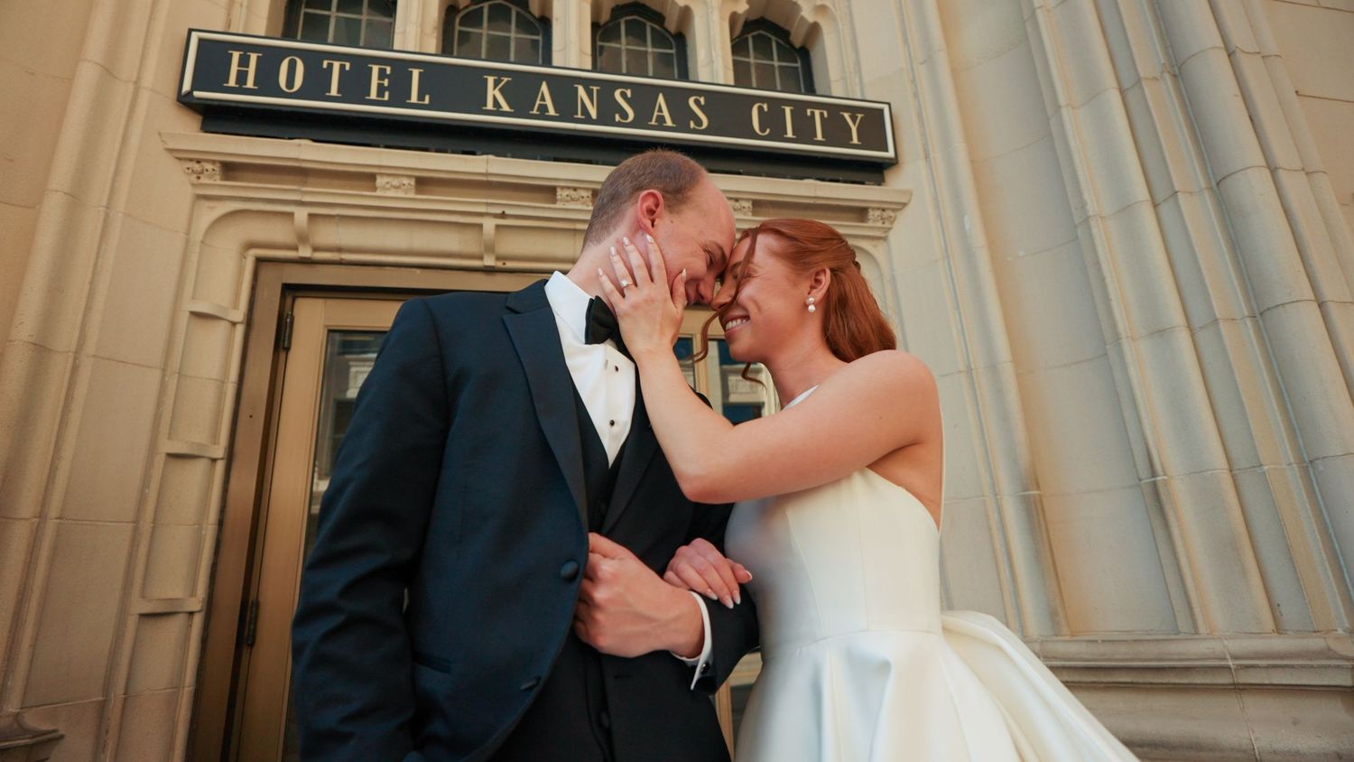 Bride and groom share romantic moment outside Hotel Kansas City, with bride in white gown and groom in navy tuxedo.