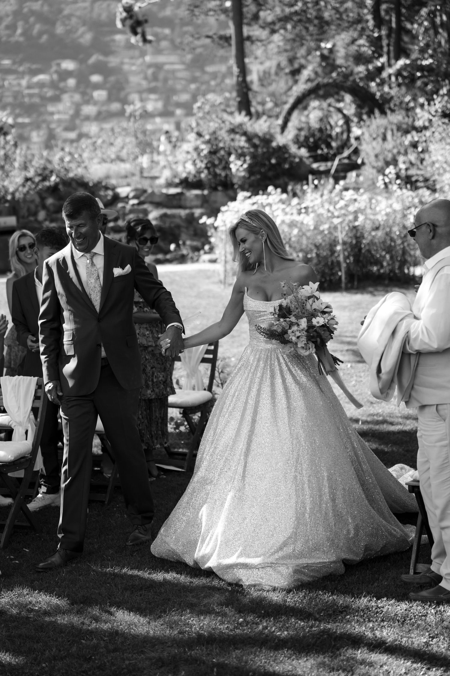 A bride in a voluminous white ballgown poses in an outdoor garden setting during a wedding celebration.