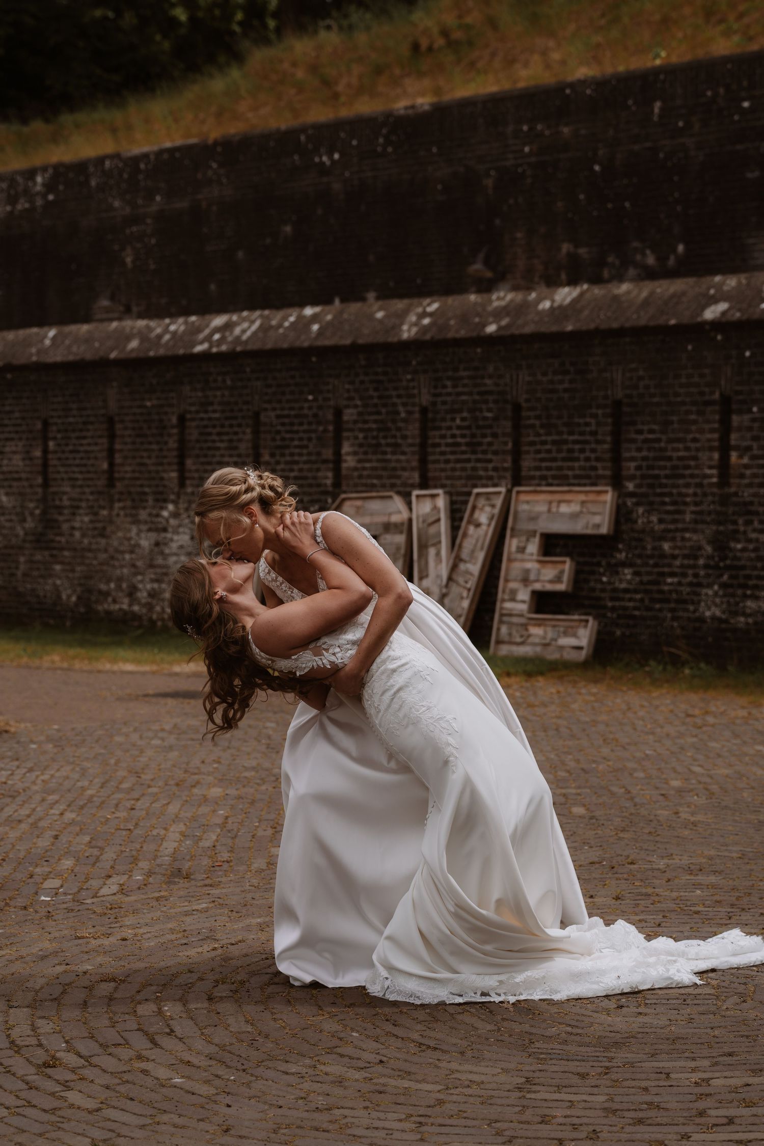 A romantic dip pose captured against a rustic brick wall background.