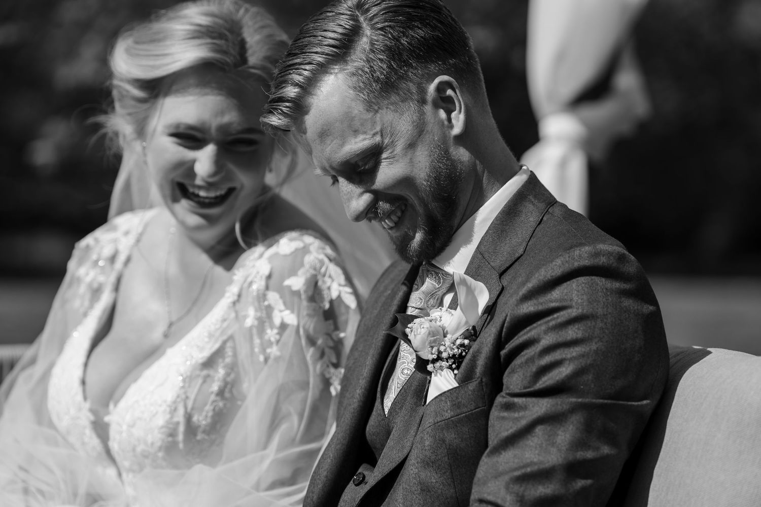 Black and white photo of a laughing bride and groom sharing a joyful moment during their wedding ceremony.