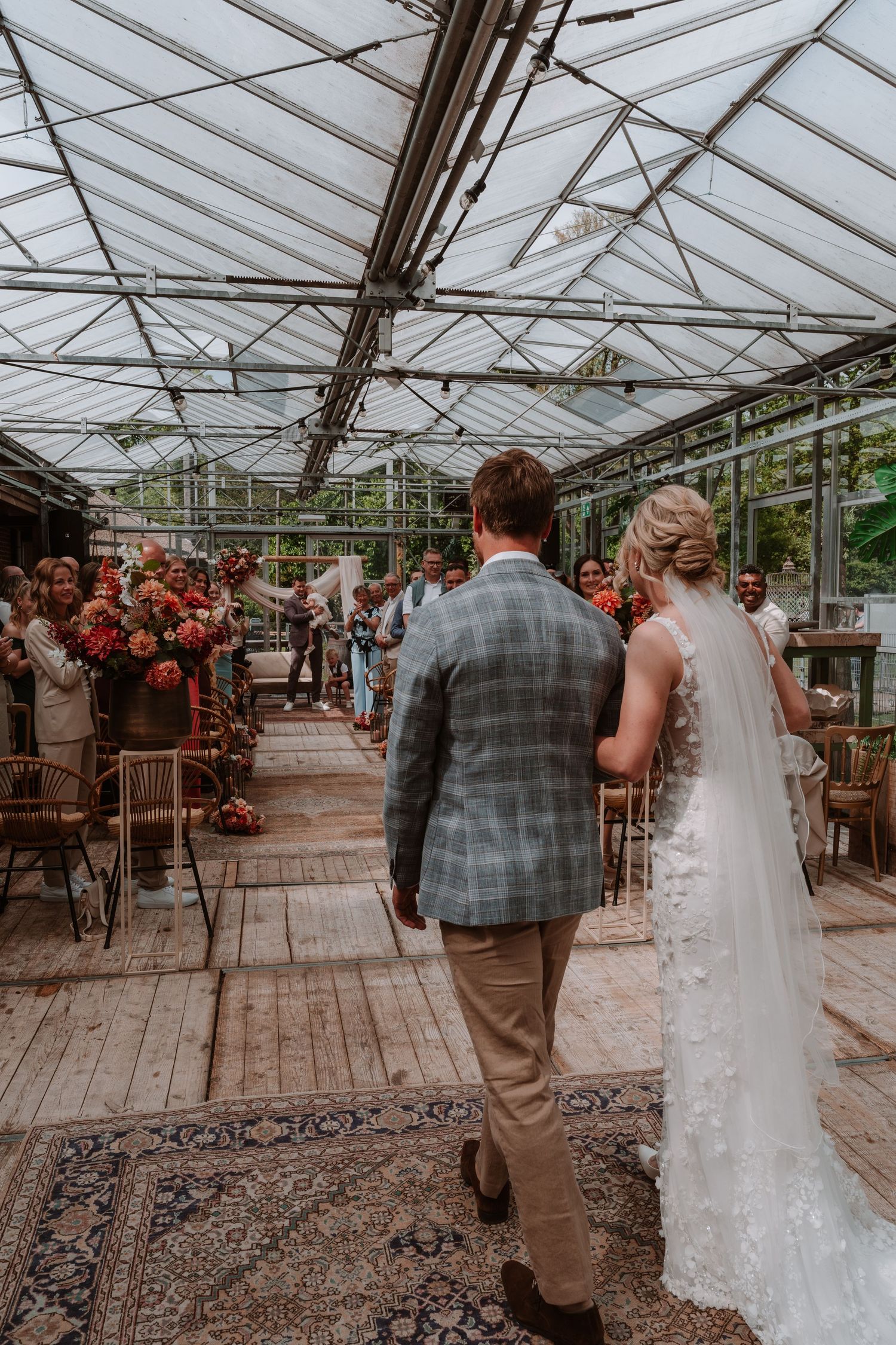 Bride and groom walk down the aisle in a stunning greenhouse wedding venue decorated with vibrant floral arrangements.
