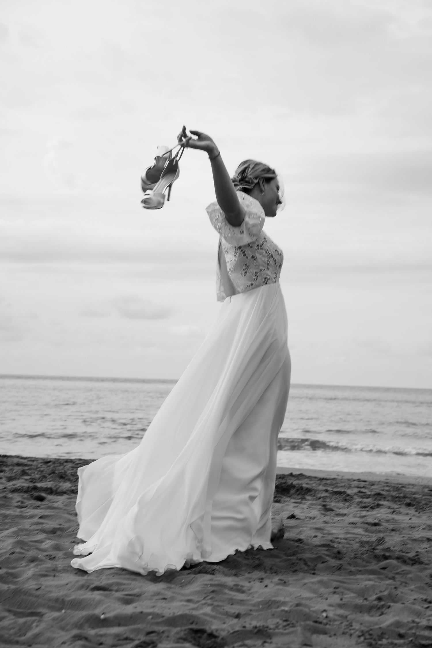 Flowing white wedding dress twirls dramatically on black sand beach.