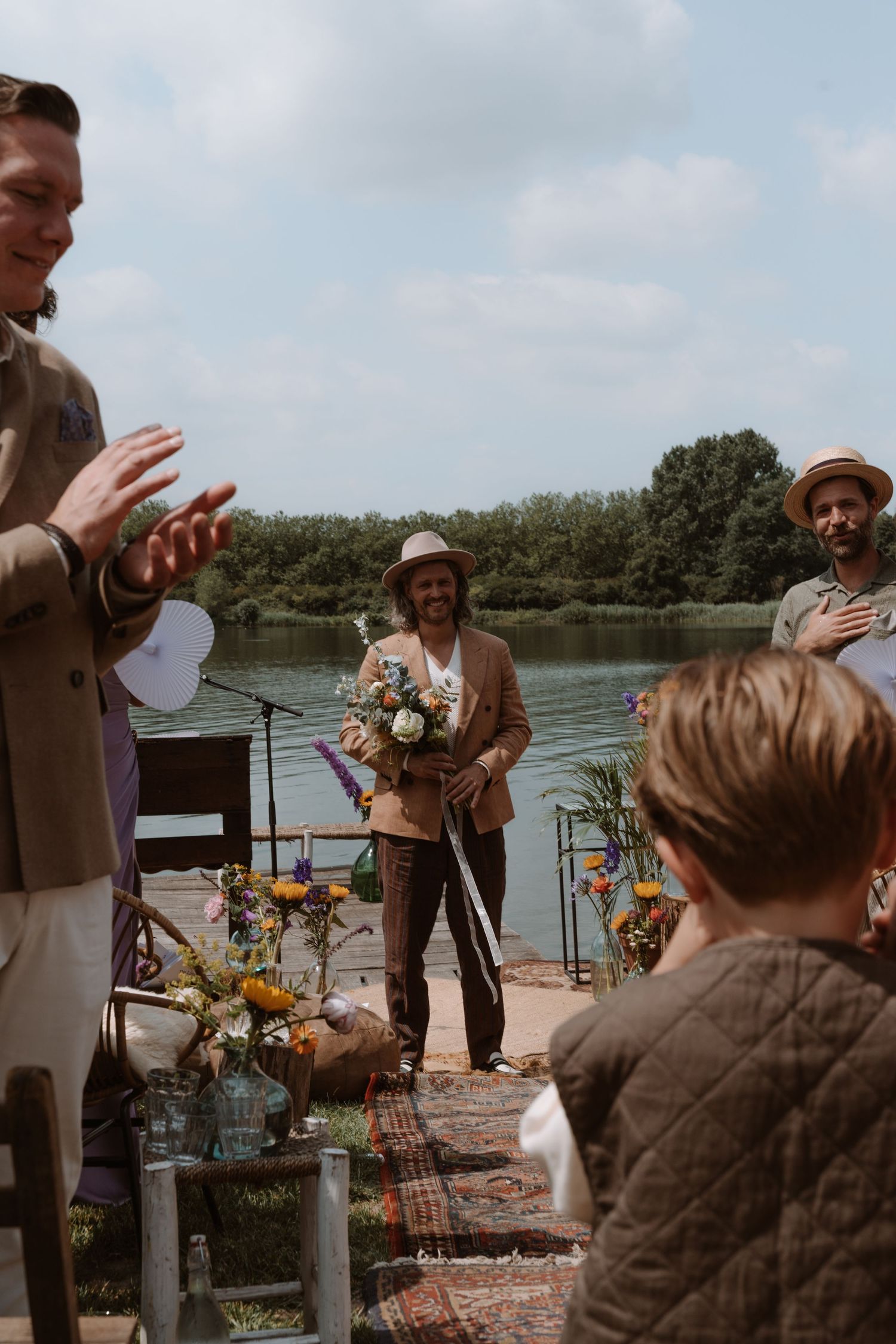 Outdoor lakeside wedding ceremony with guests and floral decorations.