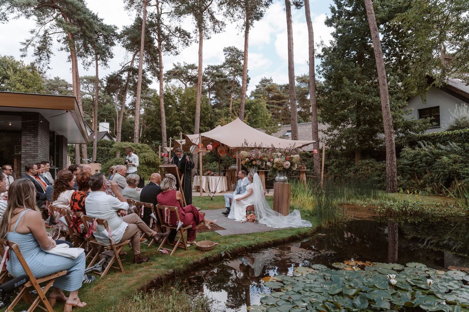 Wedding ceremony taking place in garden setting with pond and lily pads.