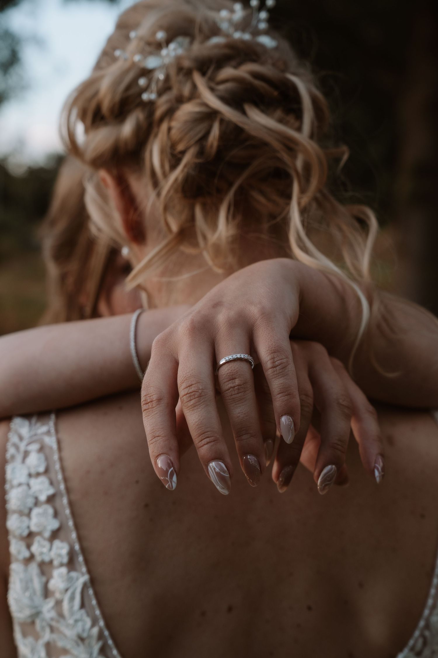 Close-up of hands with wedding ring and elegant manicure against a white lace dress.