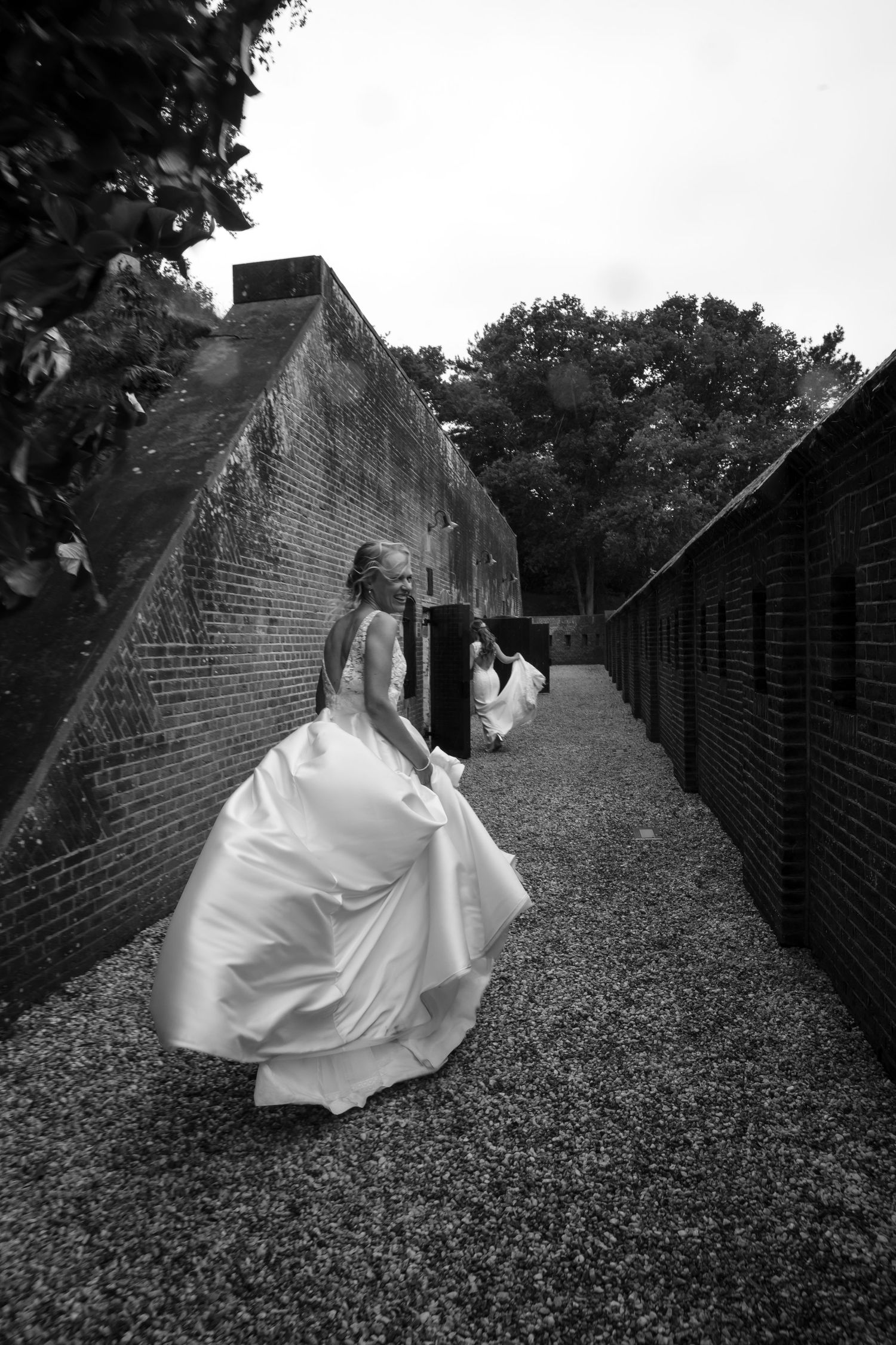A dramatic black and white photo of a flowing white wedding dress along a brick-lined path.