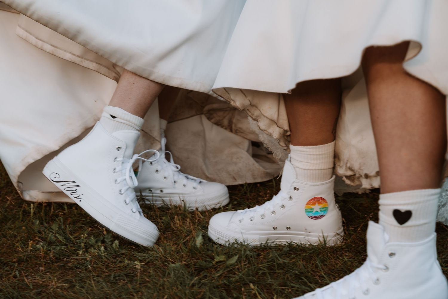 White sneakers and dress shoes worn by wedding party members on grass.