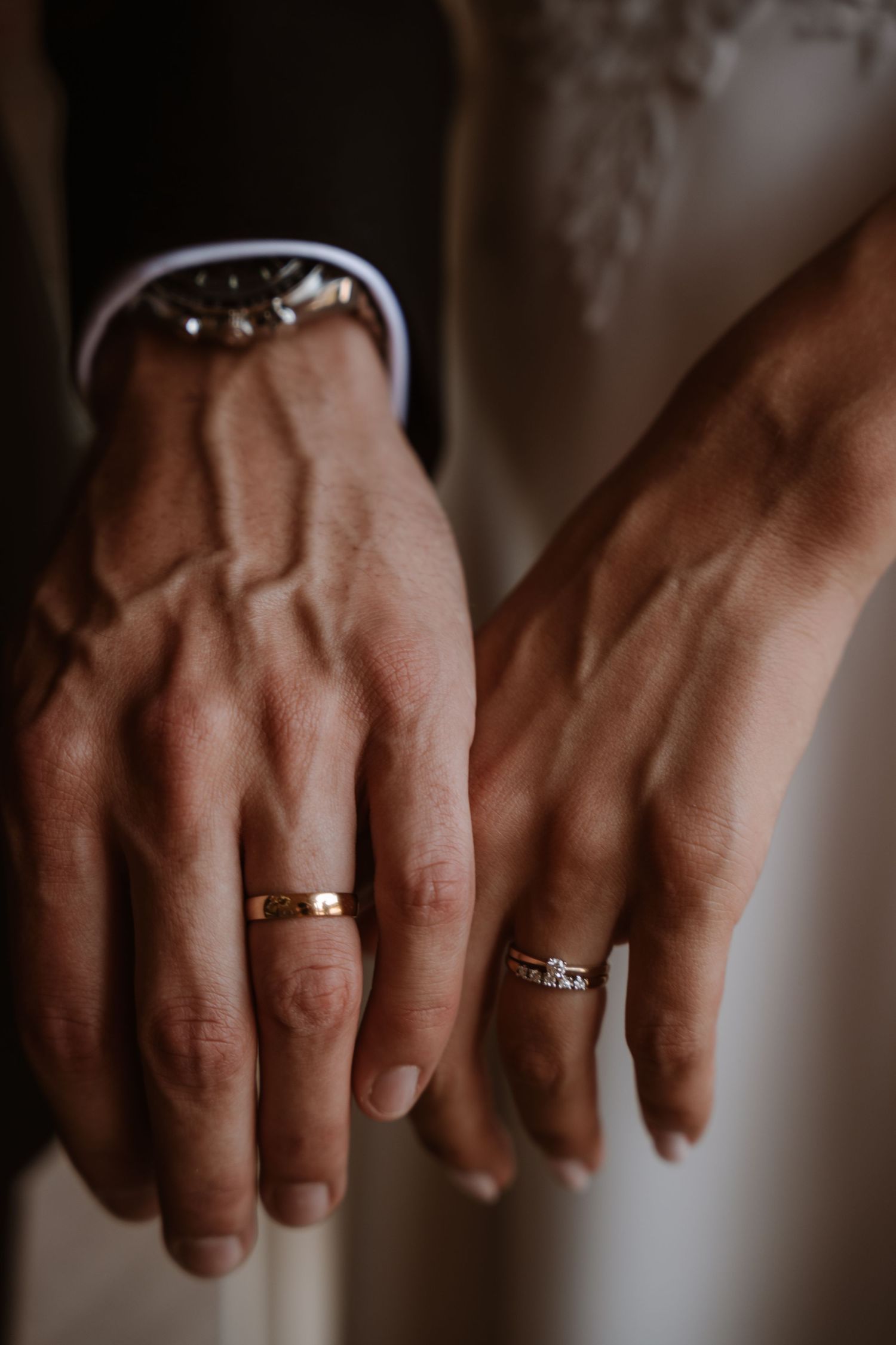 Close-up shot of hands wearing wedding rings with dramatic lighting.