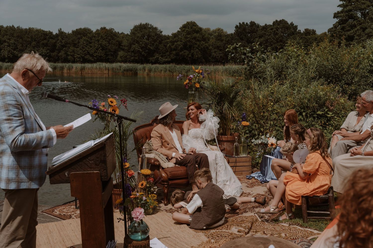 Outdoor wedding celebration with guests gathered by a lakeside venue.