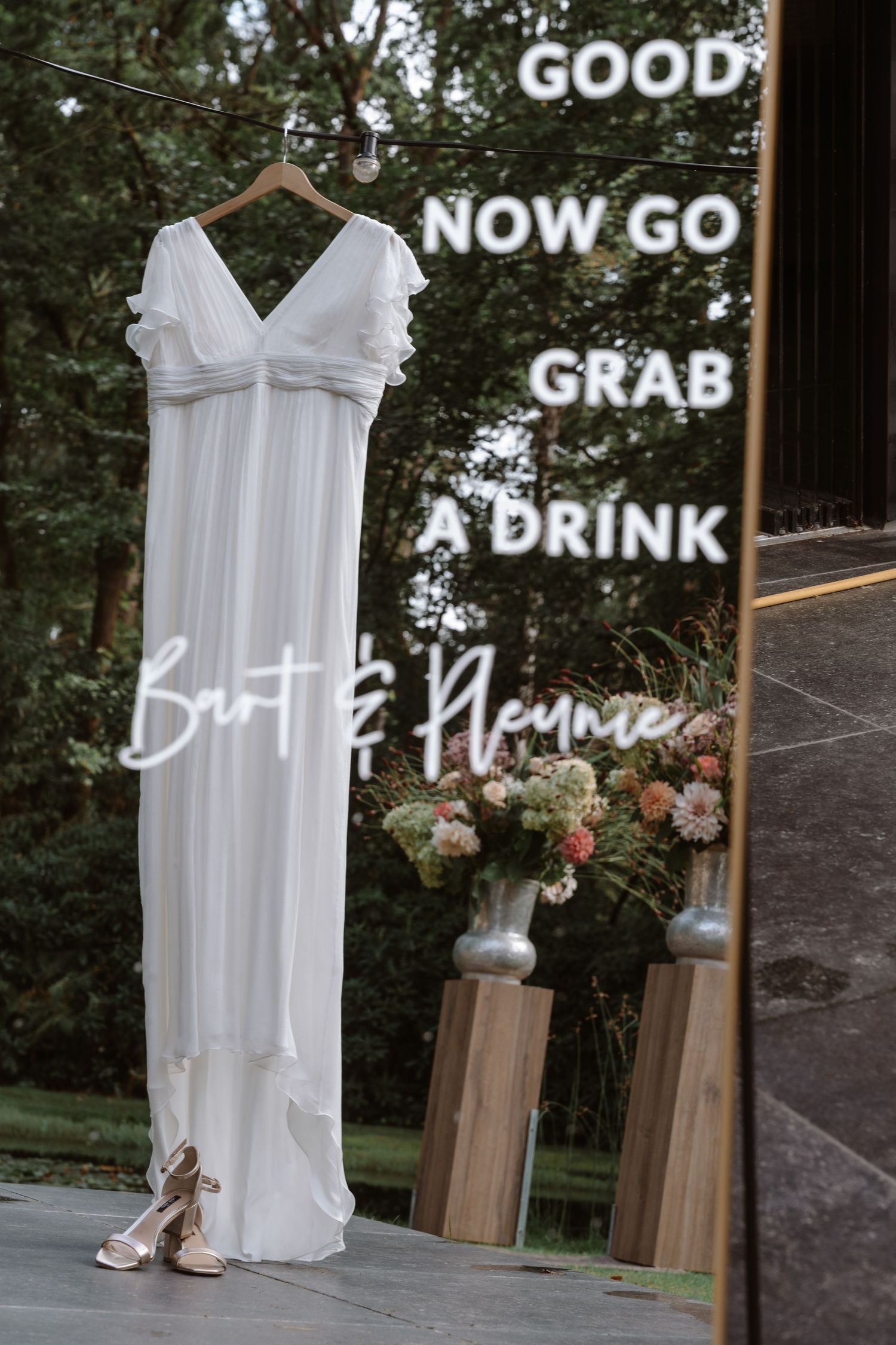 Wedding dress display with neon sign saying 'Now go grab a drink'.