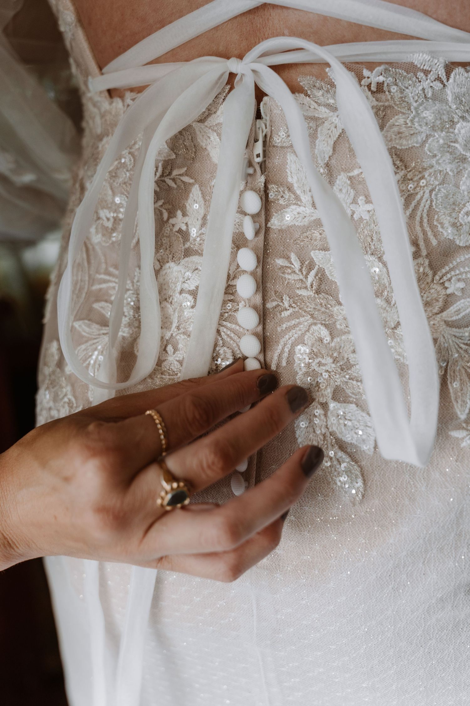 Detail shots of delicate lace and ribbon closures on a white wedding dress.