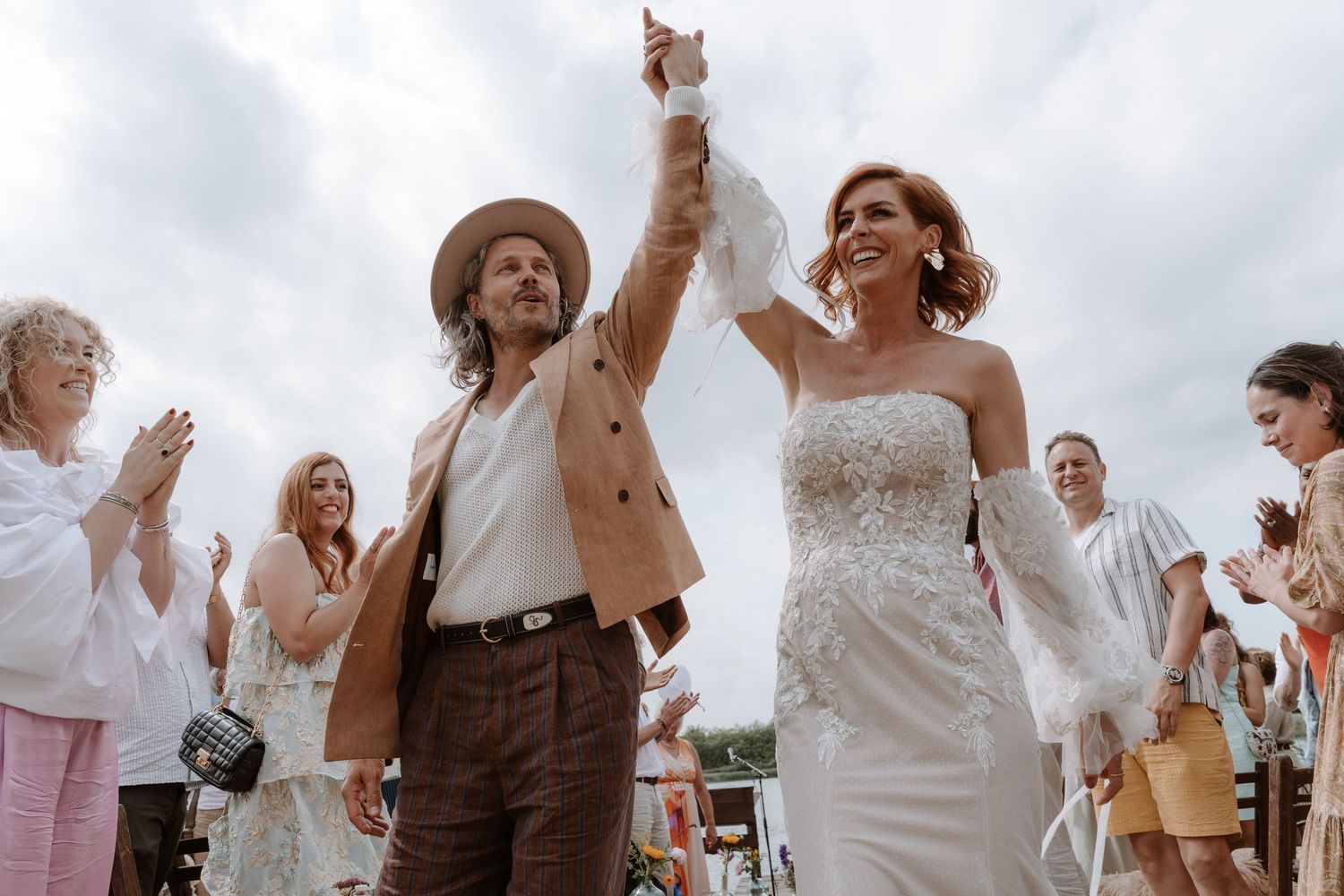 Newlyweds celebrate with raised hands during outdoor wedding reception as guests applaud.