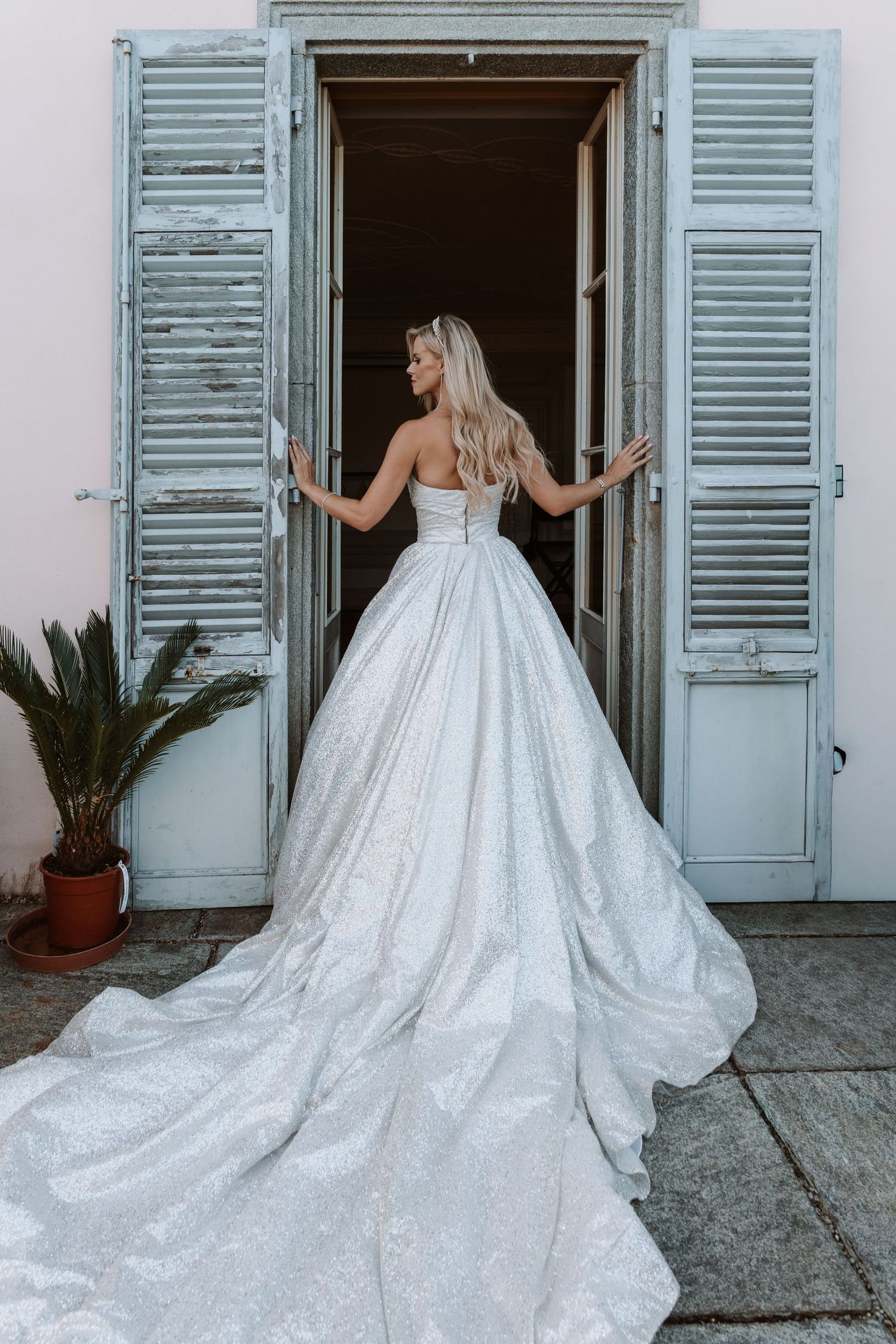 A wedding dress with a dramatic train is showcased in a sequence of photos against rustic white shuttered doors.