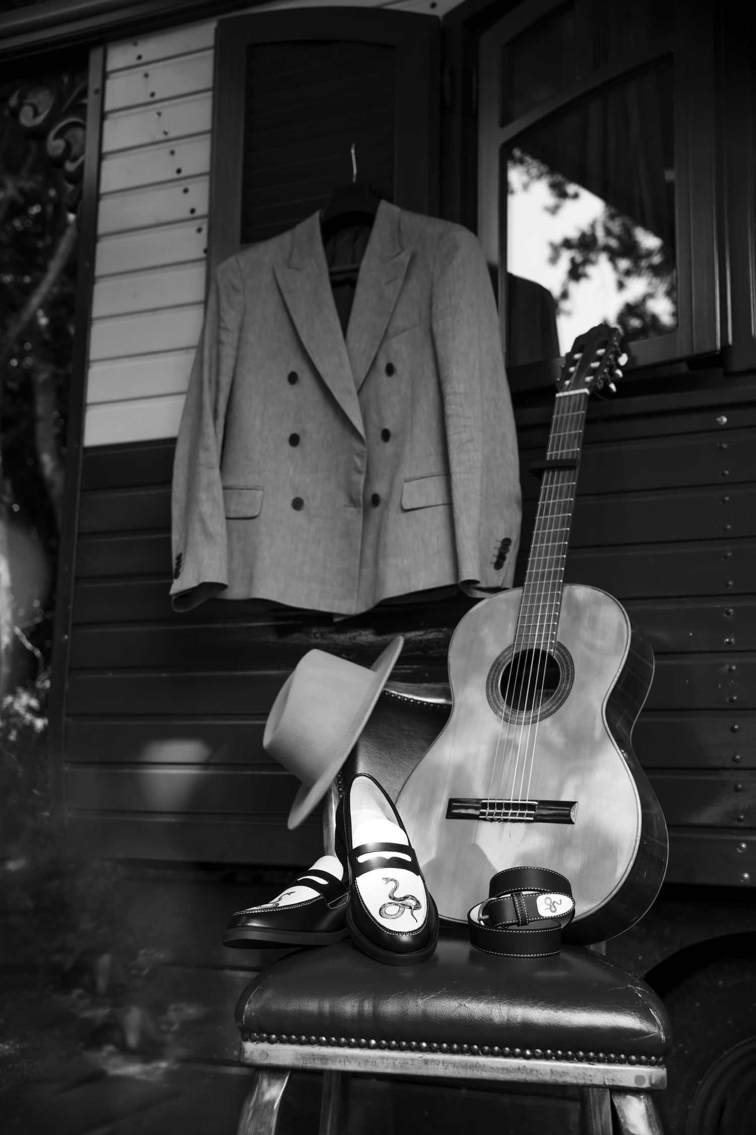 Black and white photo of acoustic guitar and formal wear arranged on bench.