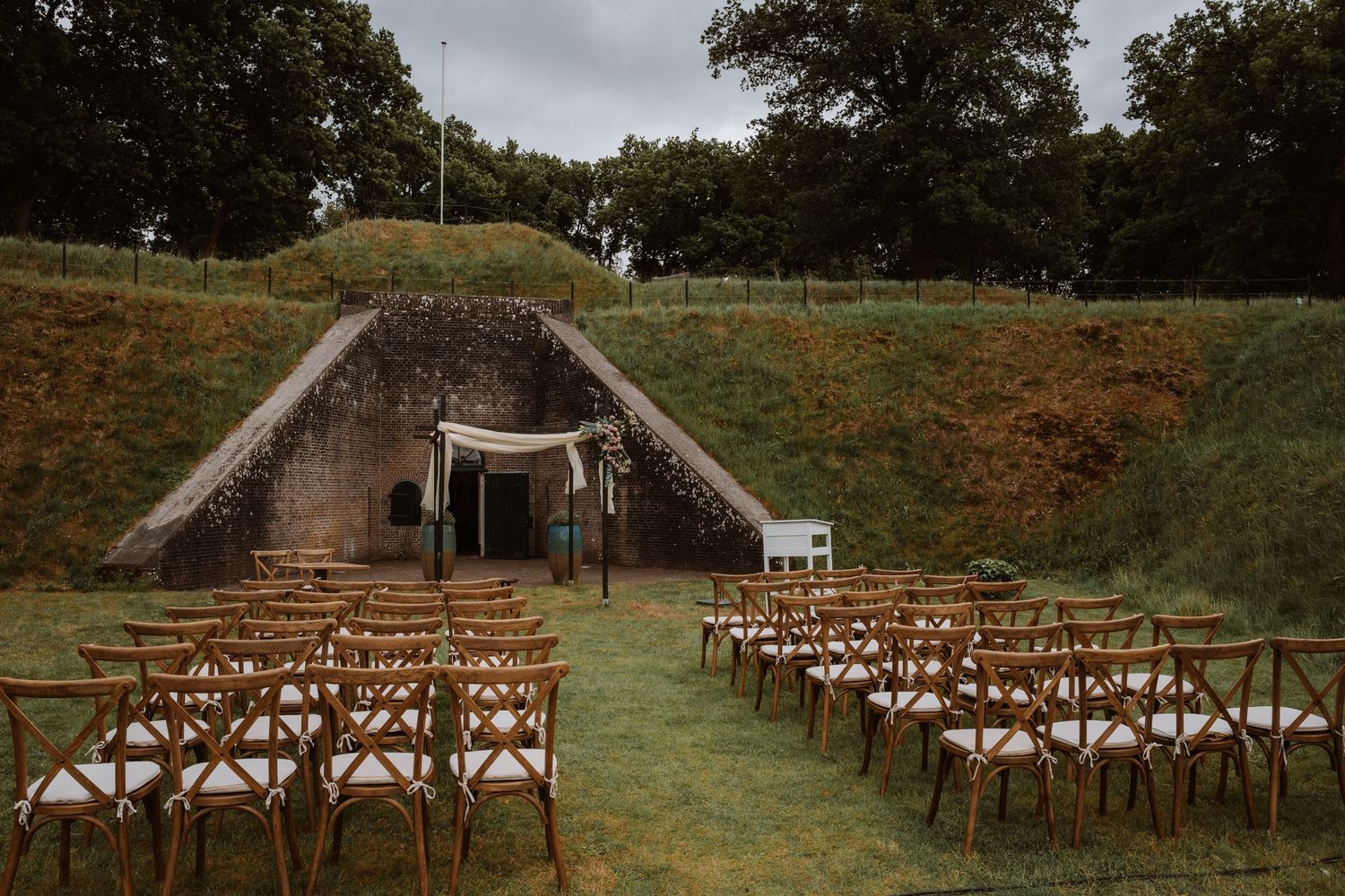 Wooden cross-back chairs set up on a grassy lawn for an outdoor wedding ceremony.