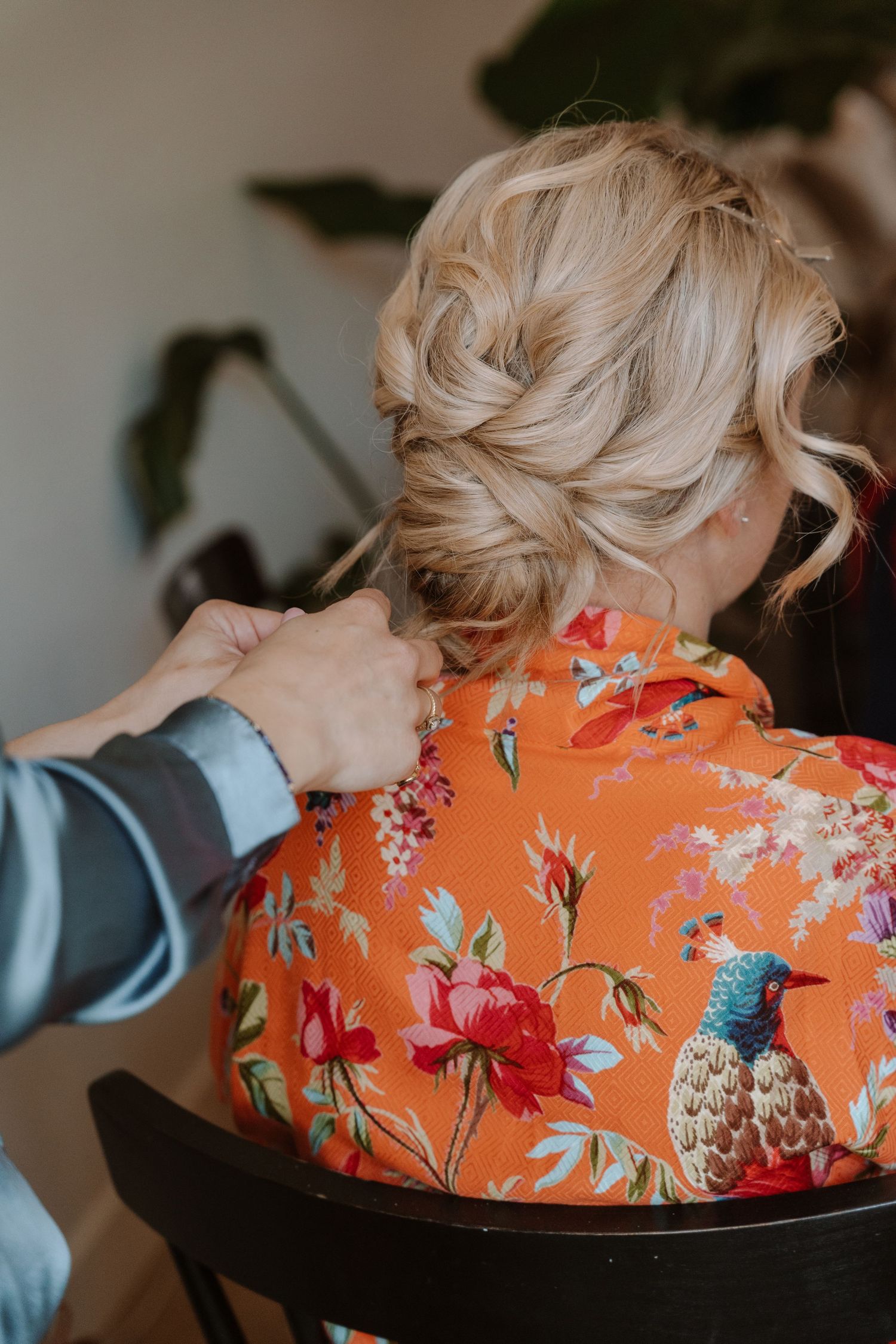 Blonde woman with elegant updo hairstyle wearing vibrant orange floral robe with hummingbird print.