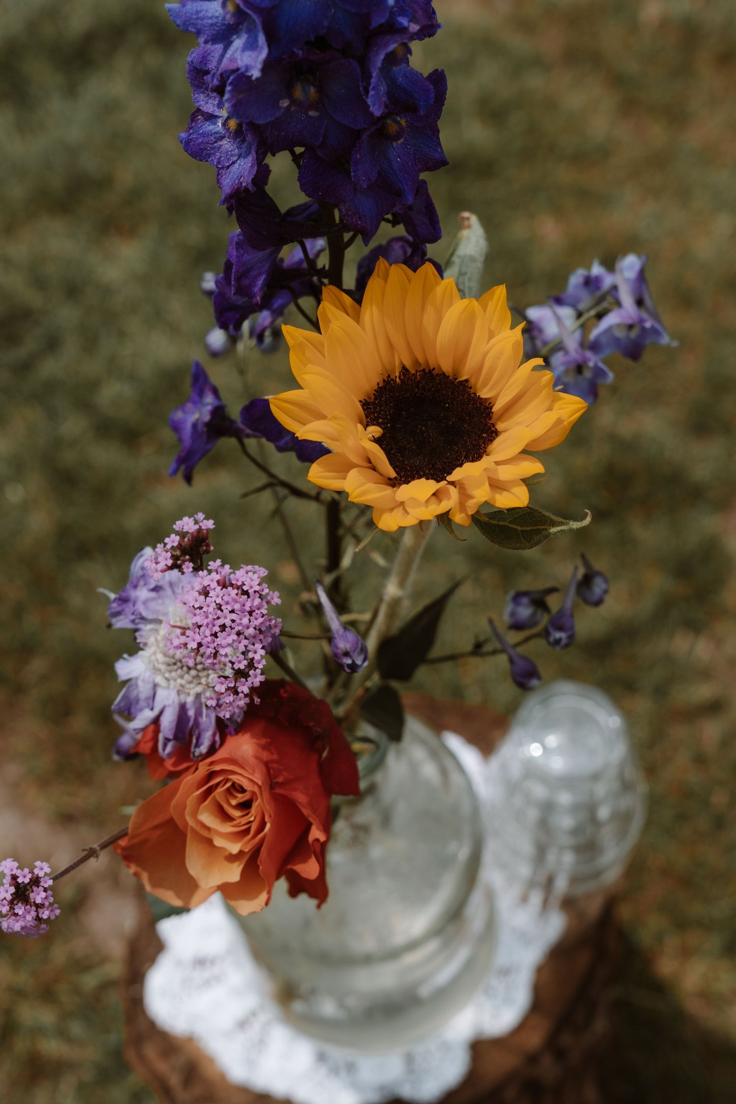 Colorful floral arrangement with purple irises and sunflowers in a delicate vase.