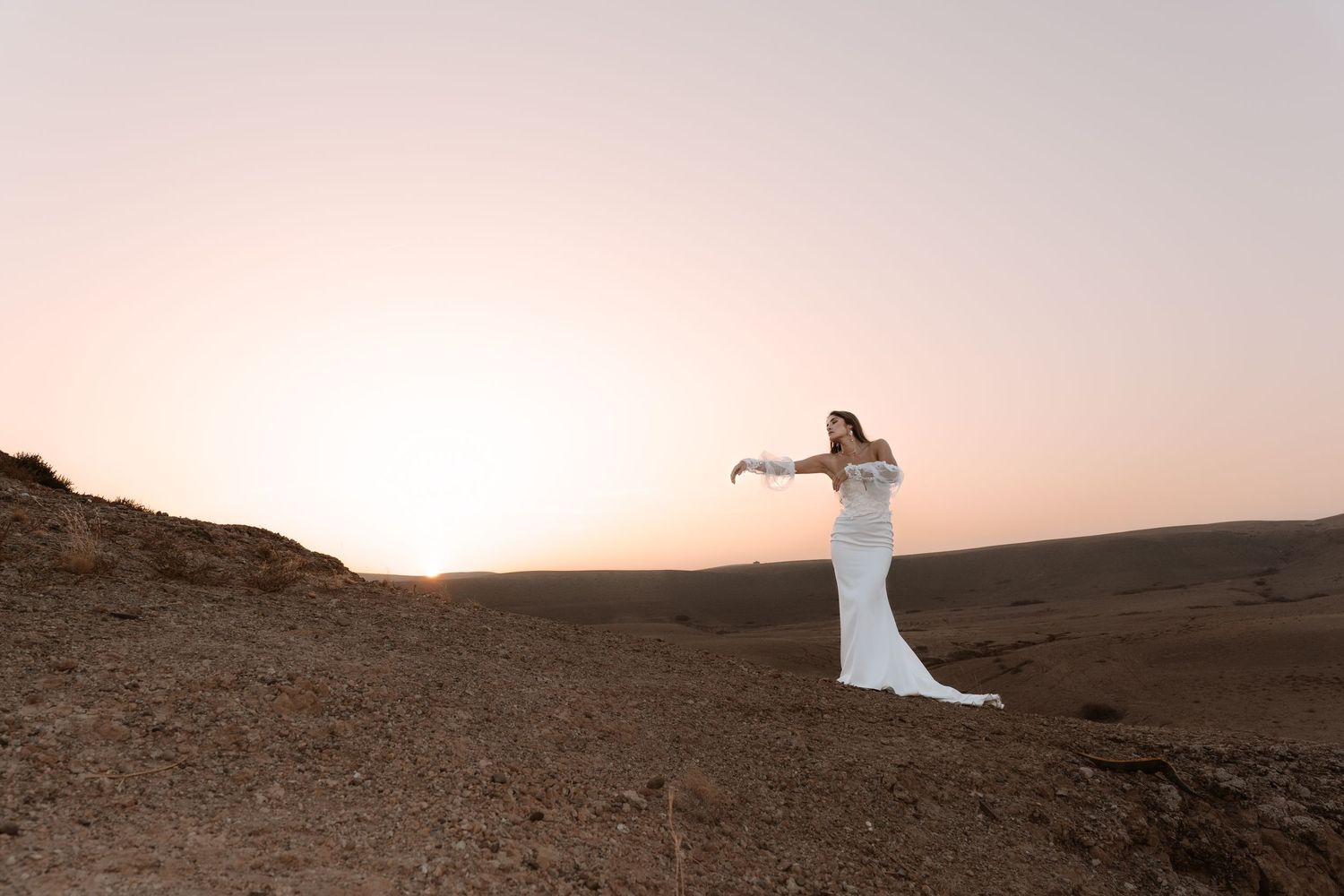 Romantic desert sunset silhouette with flowing dress against golden sky.