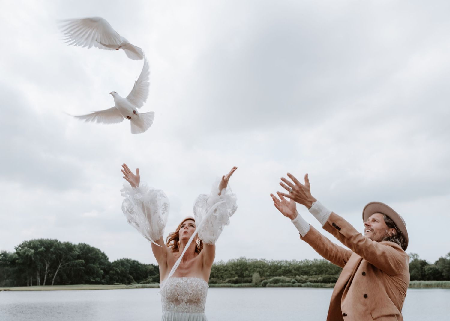 White doves being released during a lakeside wedding celebration.