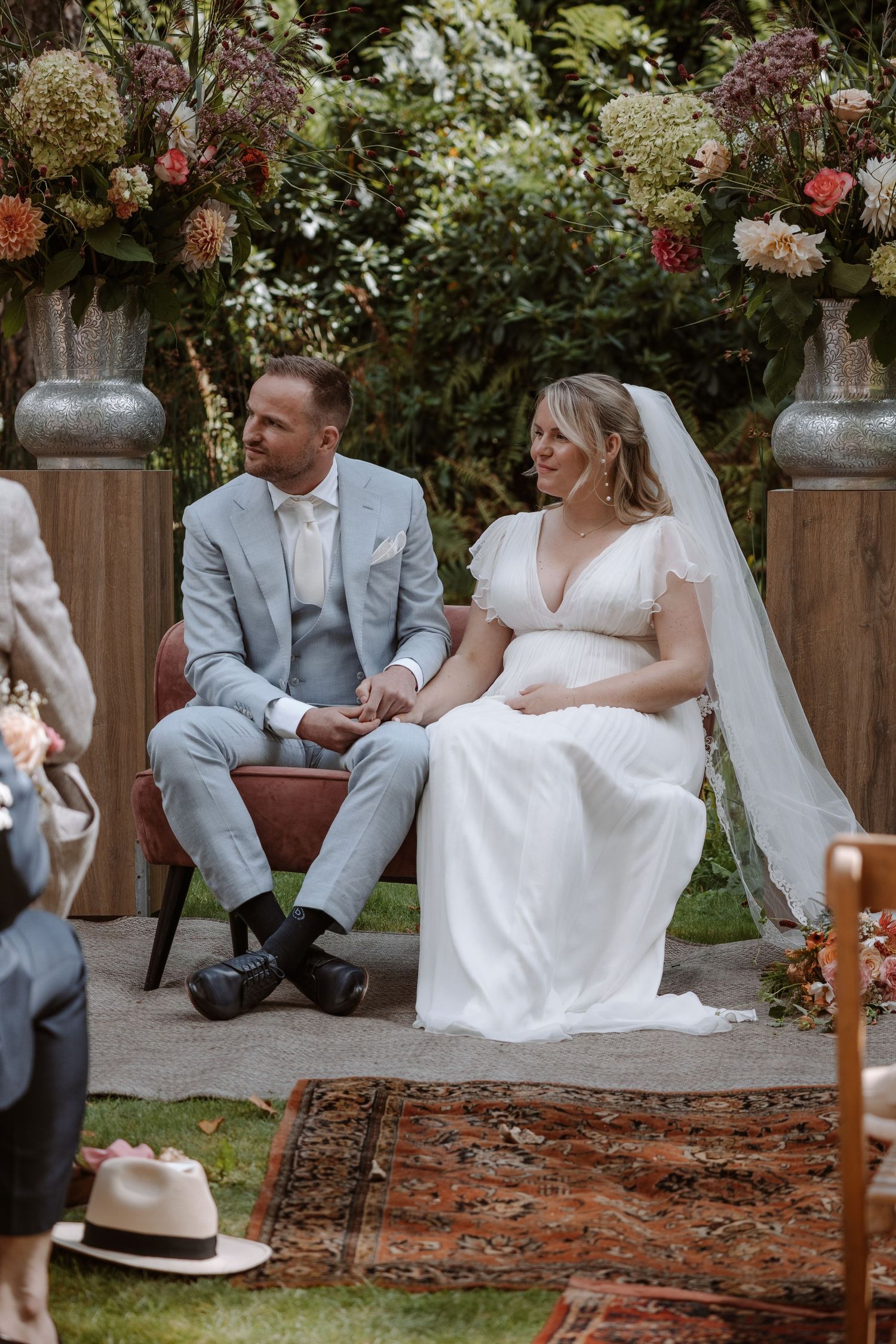 Newlyweds sitting together on chairs in a garden setting with floral decorations.