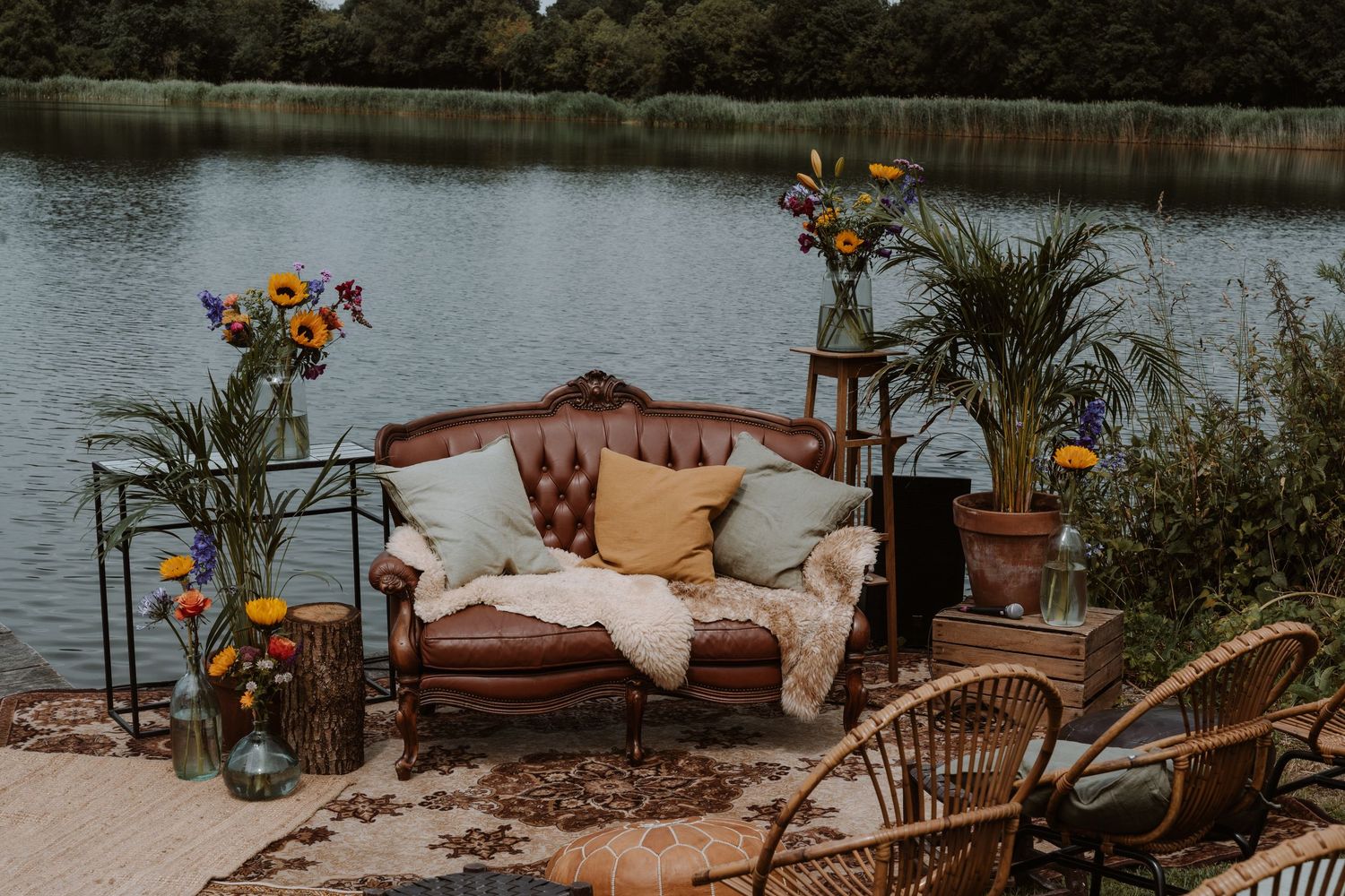 Waterfront lounge setup with wicker furniture and colorful floral arrangements by a lake.