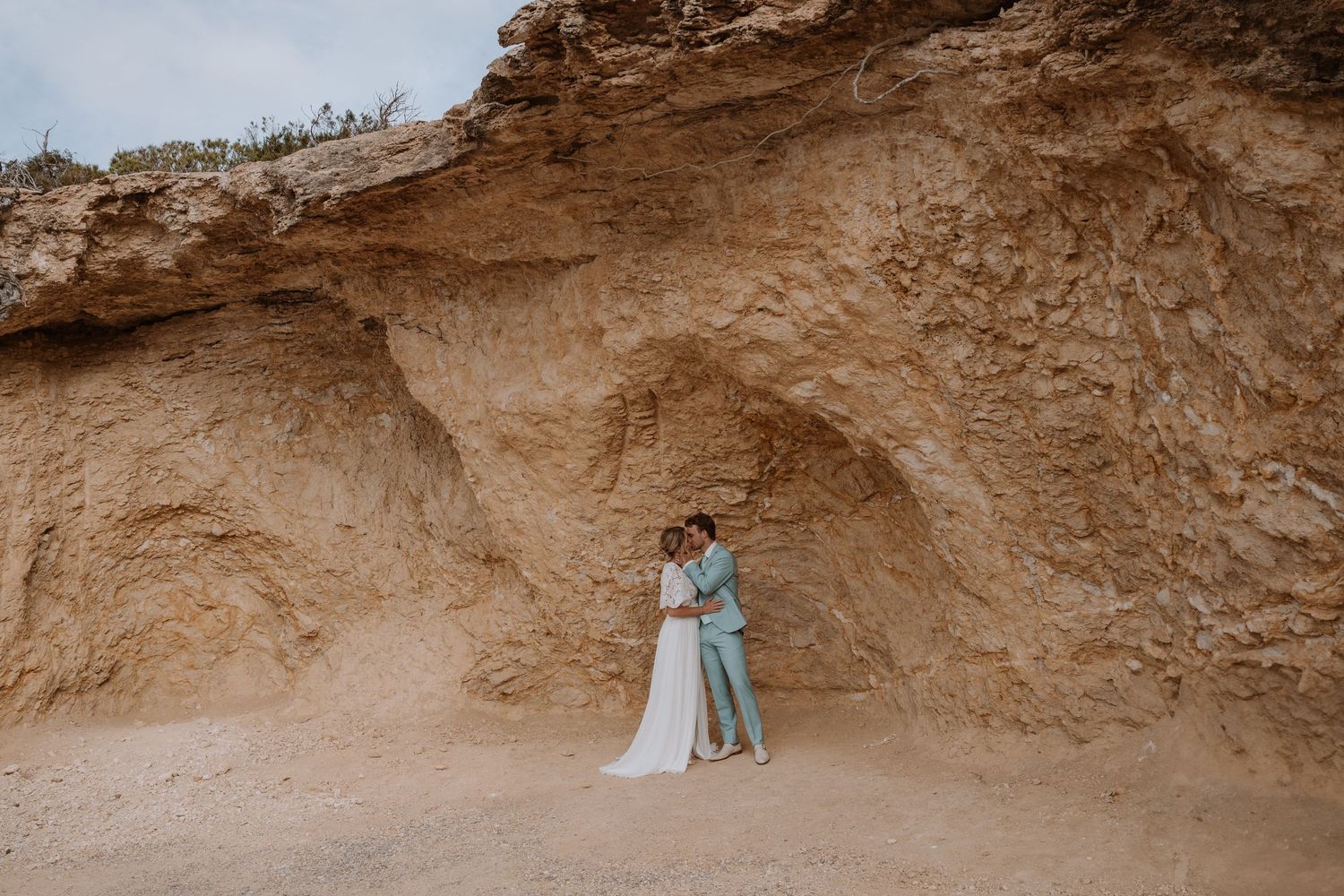 Wedding couple poses in romantic cliffside setting with natural rock formations.