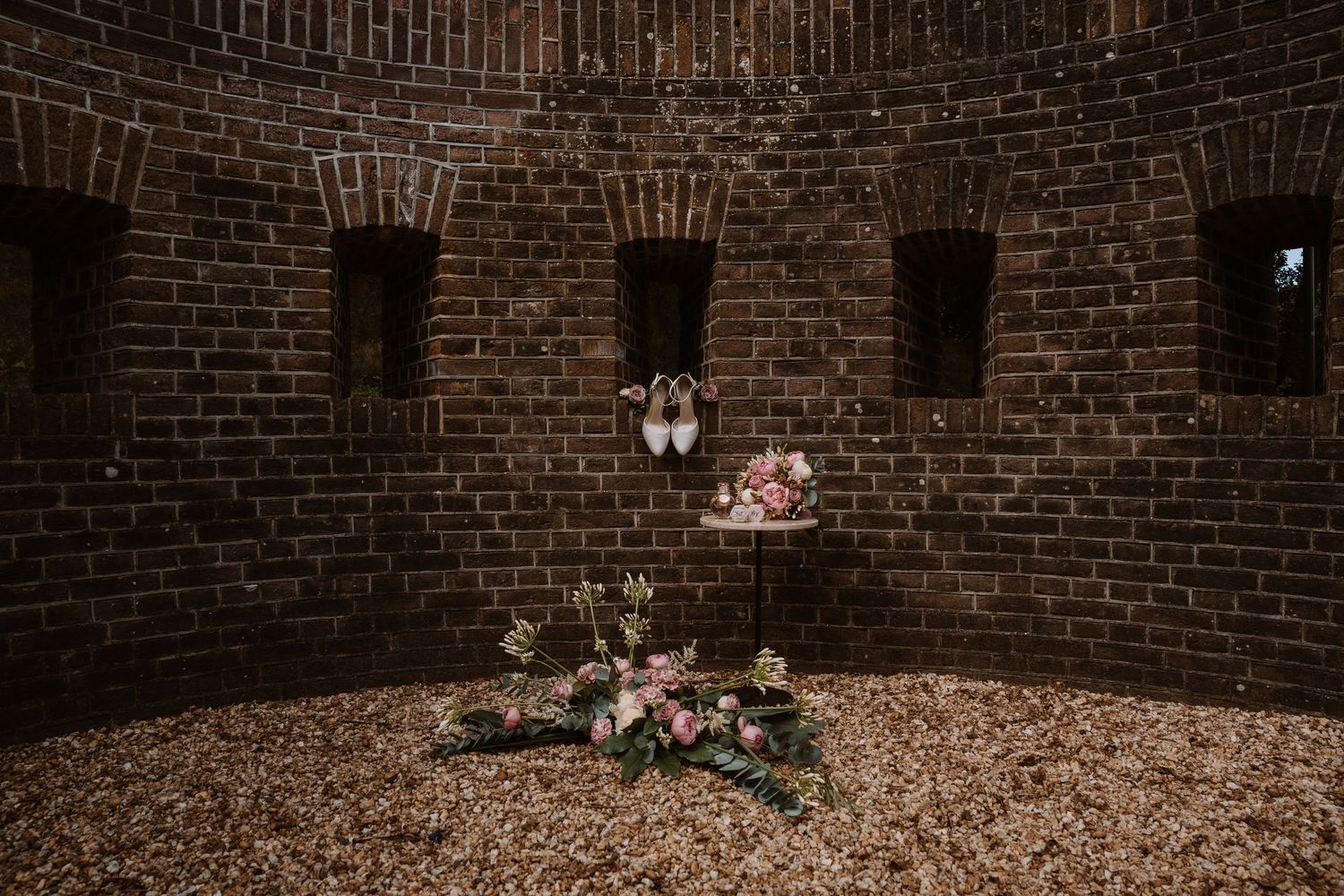 A rustic brick archway decorated with delicate floral arrangements for a wedding ceremony.