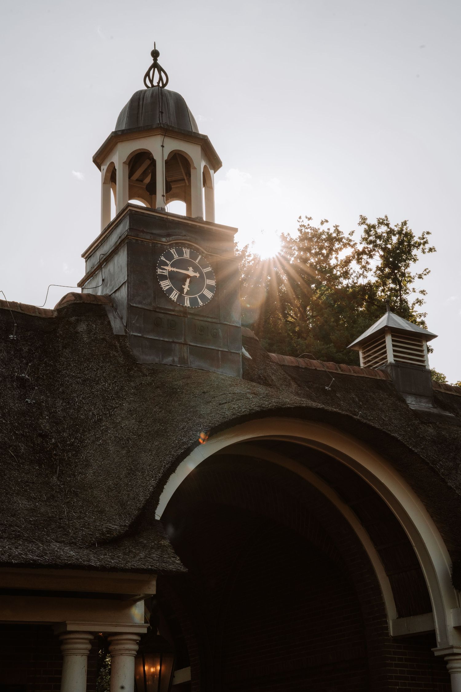 Sunlight peeks through an architectural arch with a domed cupola at sunset.