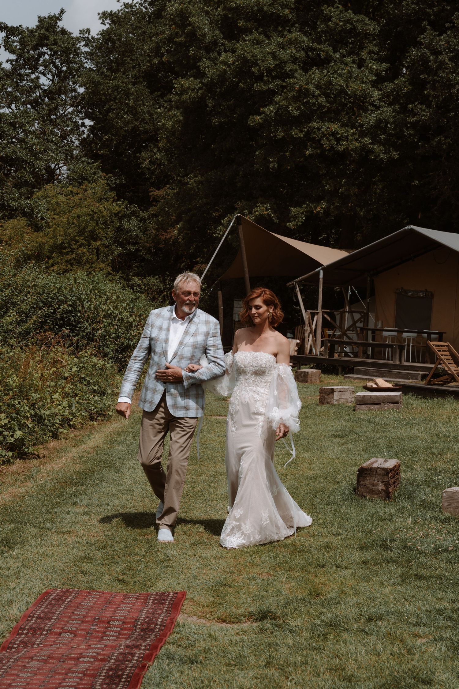 Wedding couple walking together on grass with rustic cabins in the background.