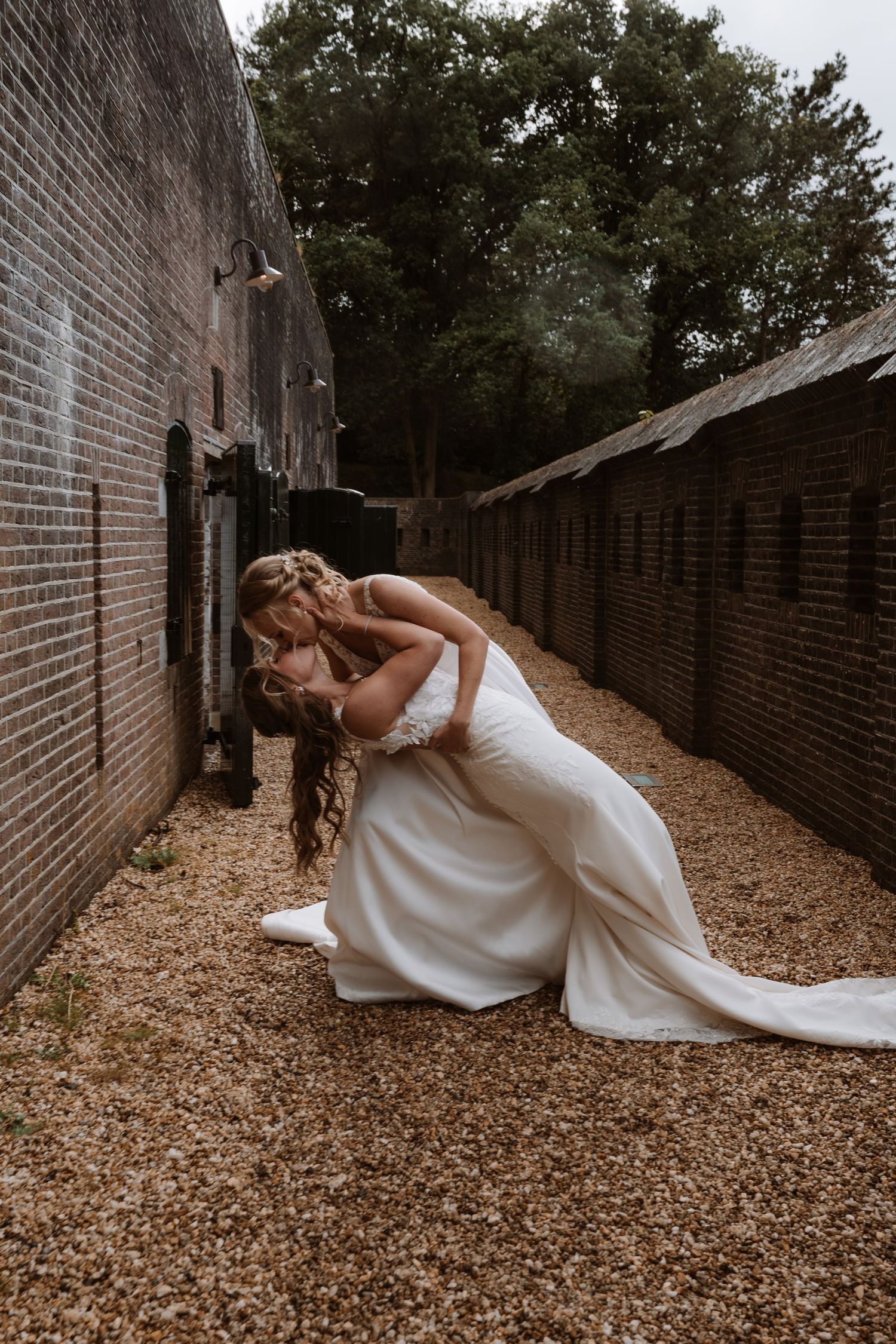 A white wedding dress flows elegantly against a rustic brick wall backdrop.