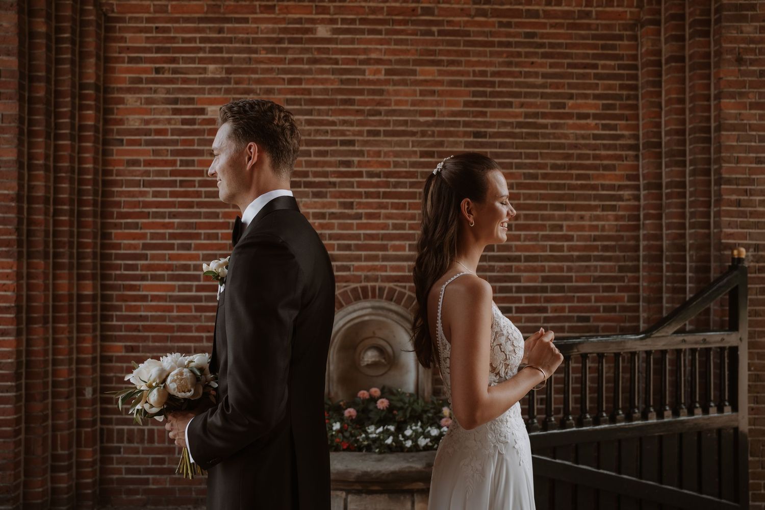 Wedding couple photographed from behind in an elegant brick-walled venue setting.