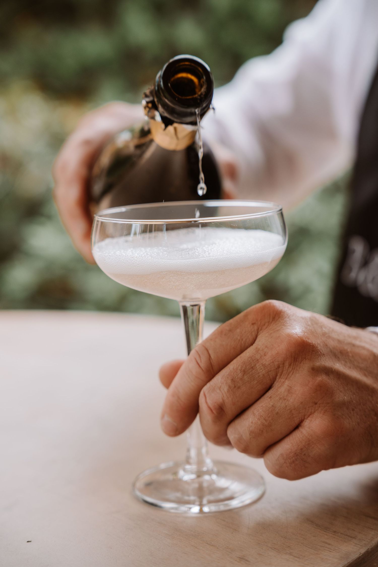 Champagne being poured into coupe glass by server at event.