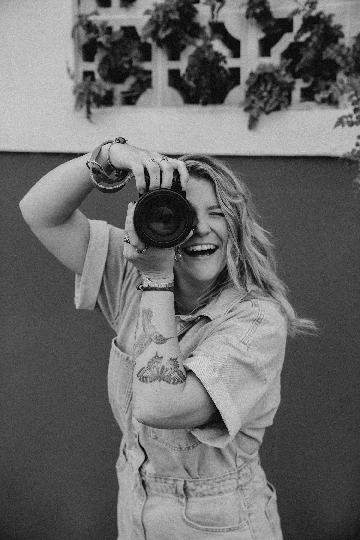 Black and white photo of photographer in denim overalls taking pictures with vintage camera.