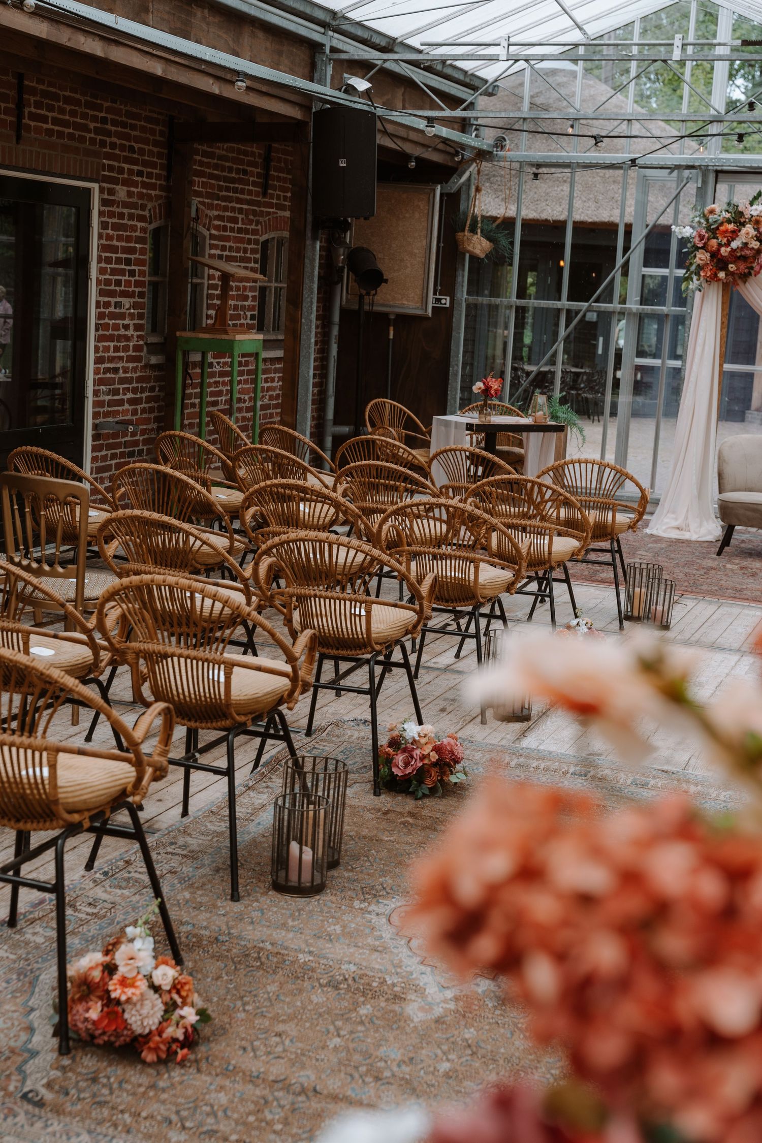 Rattan chairs arranged for an outdoor wedding ceremony beside a brick building with floral decorations.