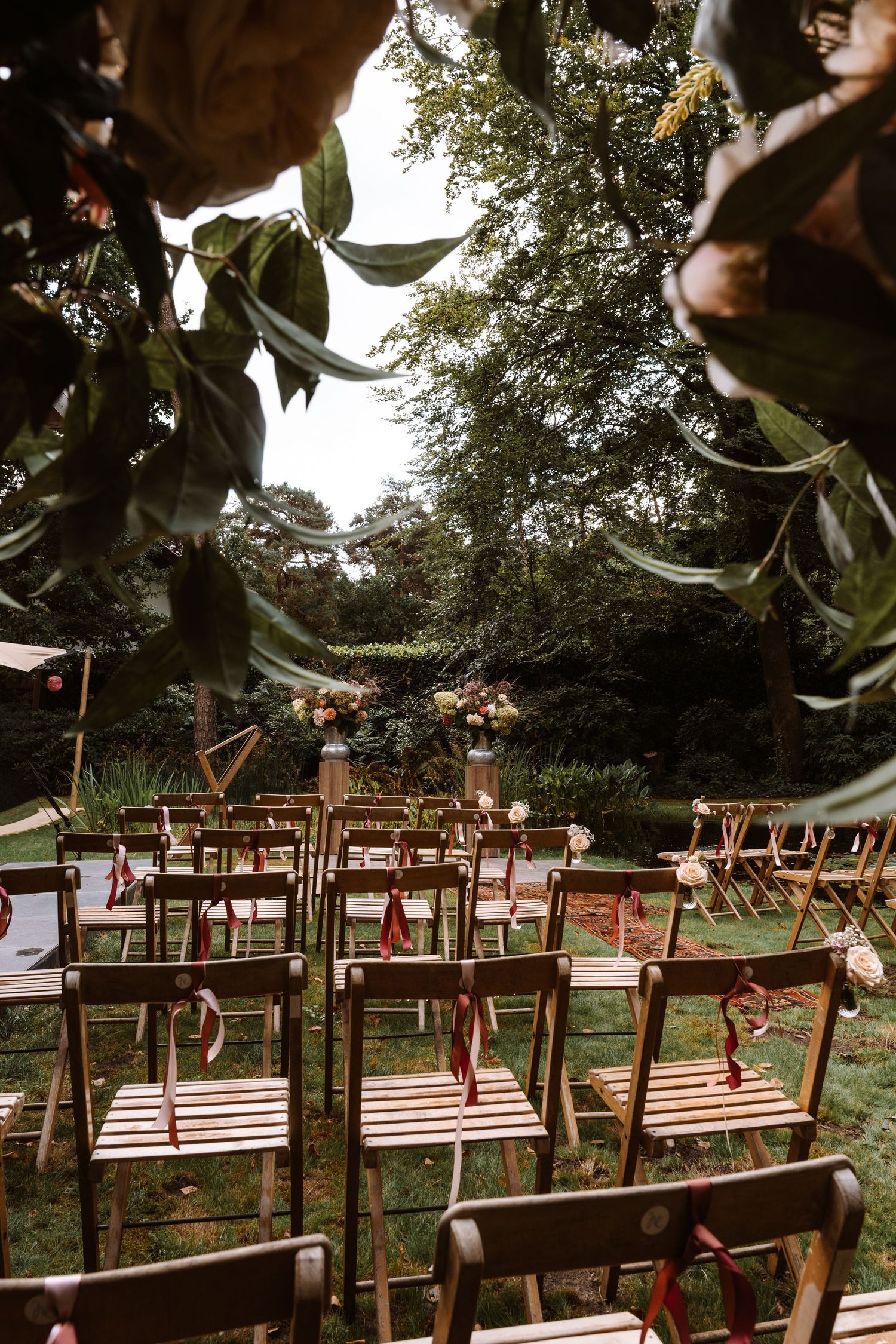 Outdoor wedding ceremony setup with wooden chairs arranged in rows under trees.