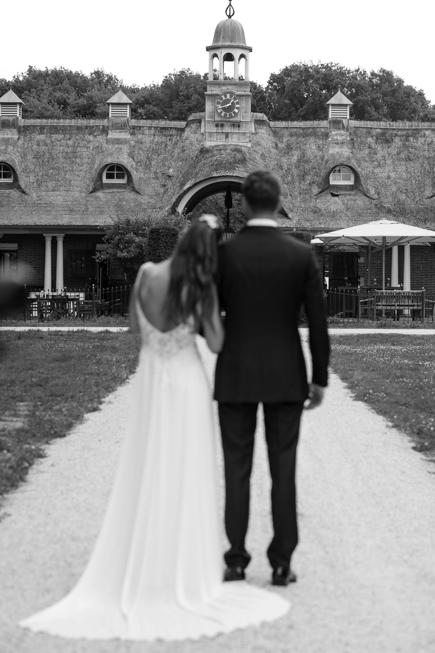 Black and white photo of newlyweds walking away together on path in front of historic stone building.