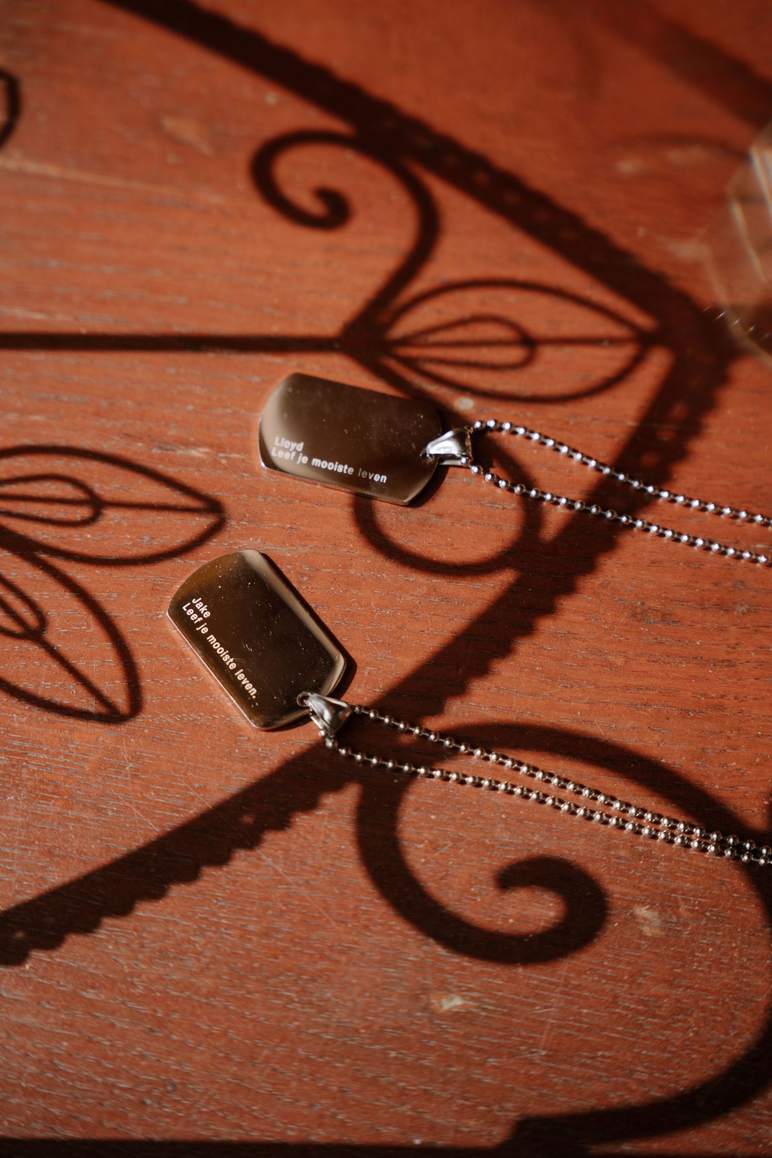 Dog tags casting intricate shadow patterns on wooden surface.