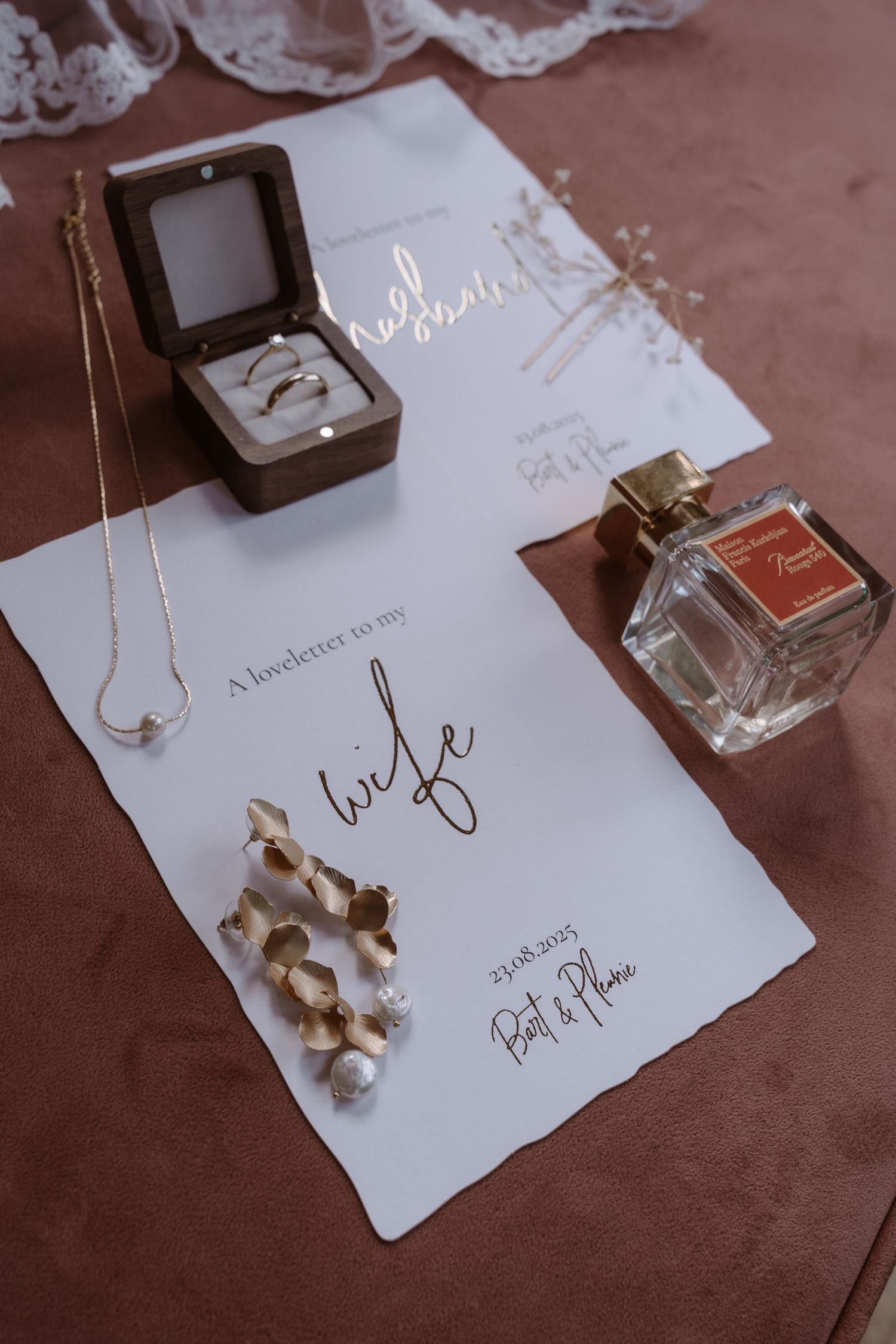 Wedding stationery and accessories artfully arranged on a brown surface.