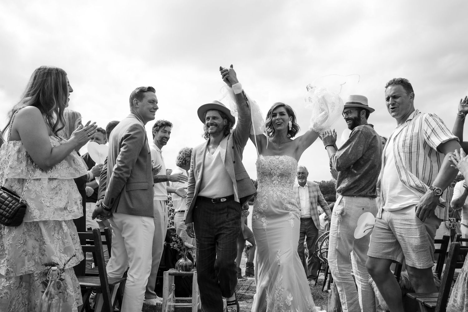 Black and white photo of wedding guests celebrating outdoors with raised hands.