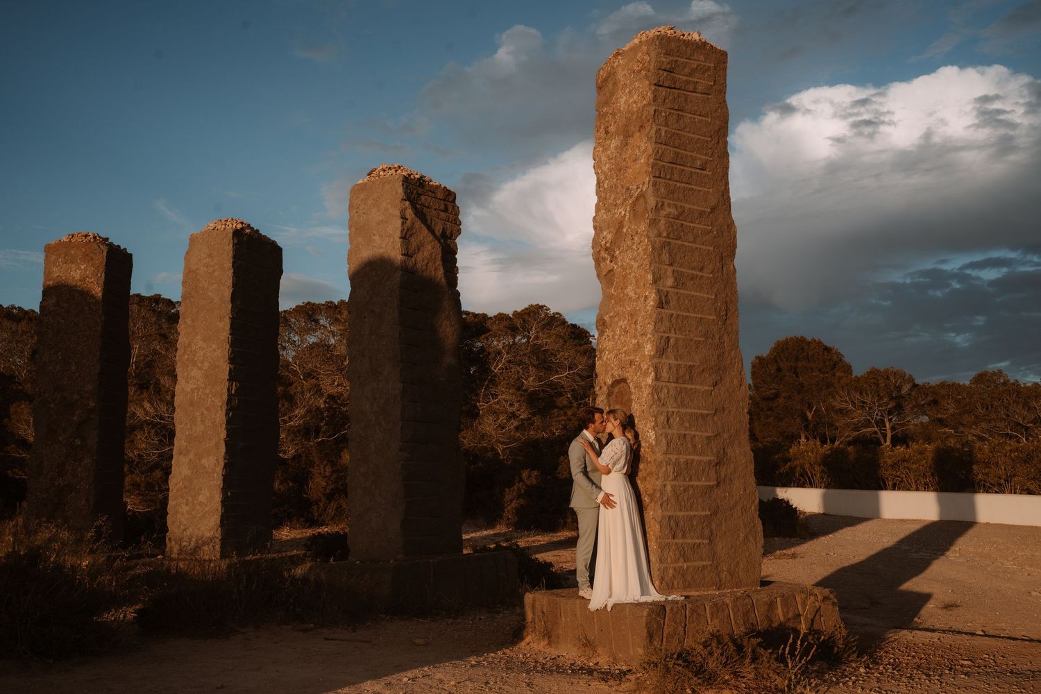 Ancient stone pillars stand against a dramatic sky at sunset.