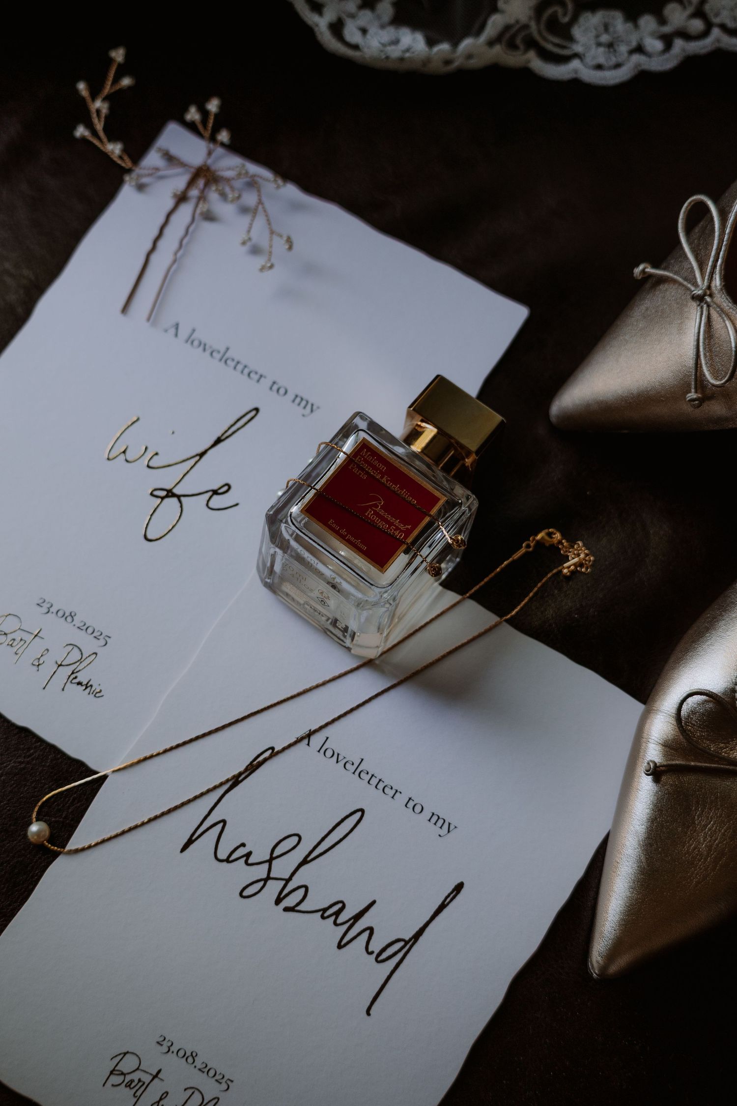 Wedding stationery and perfume bottle styled with elegant calligraphy on dark background.