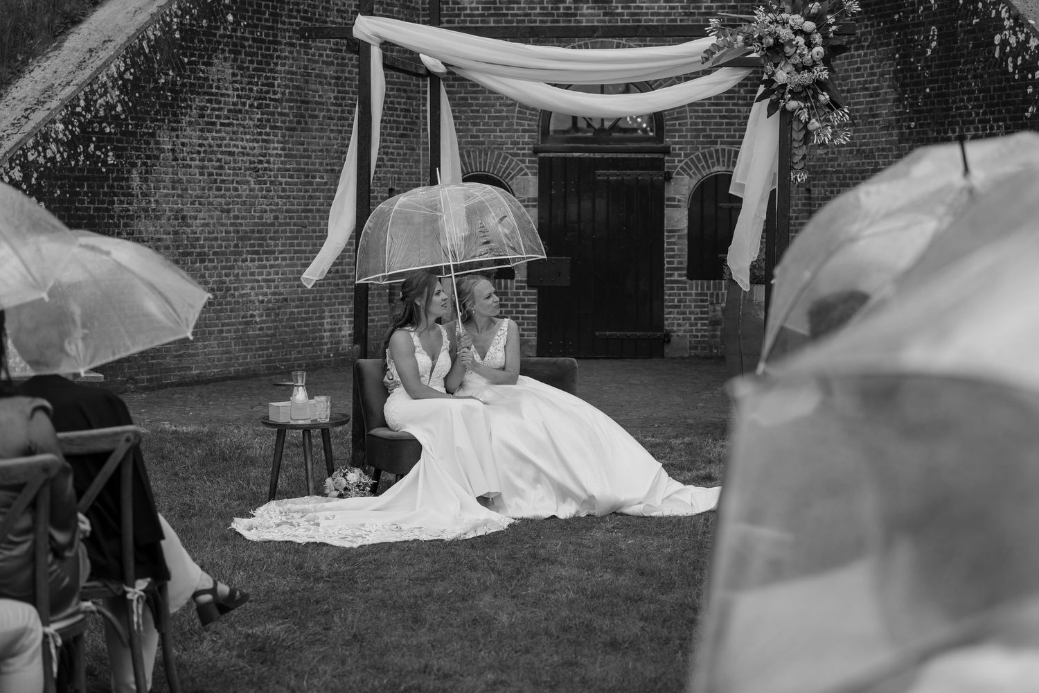 A black and white photo of a wedding ceremony under a draped canopy with umbrellas in the foreground.