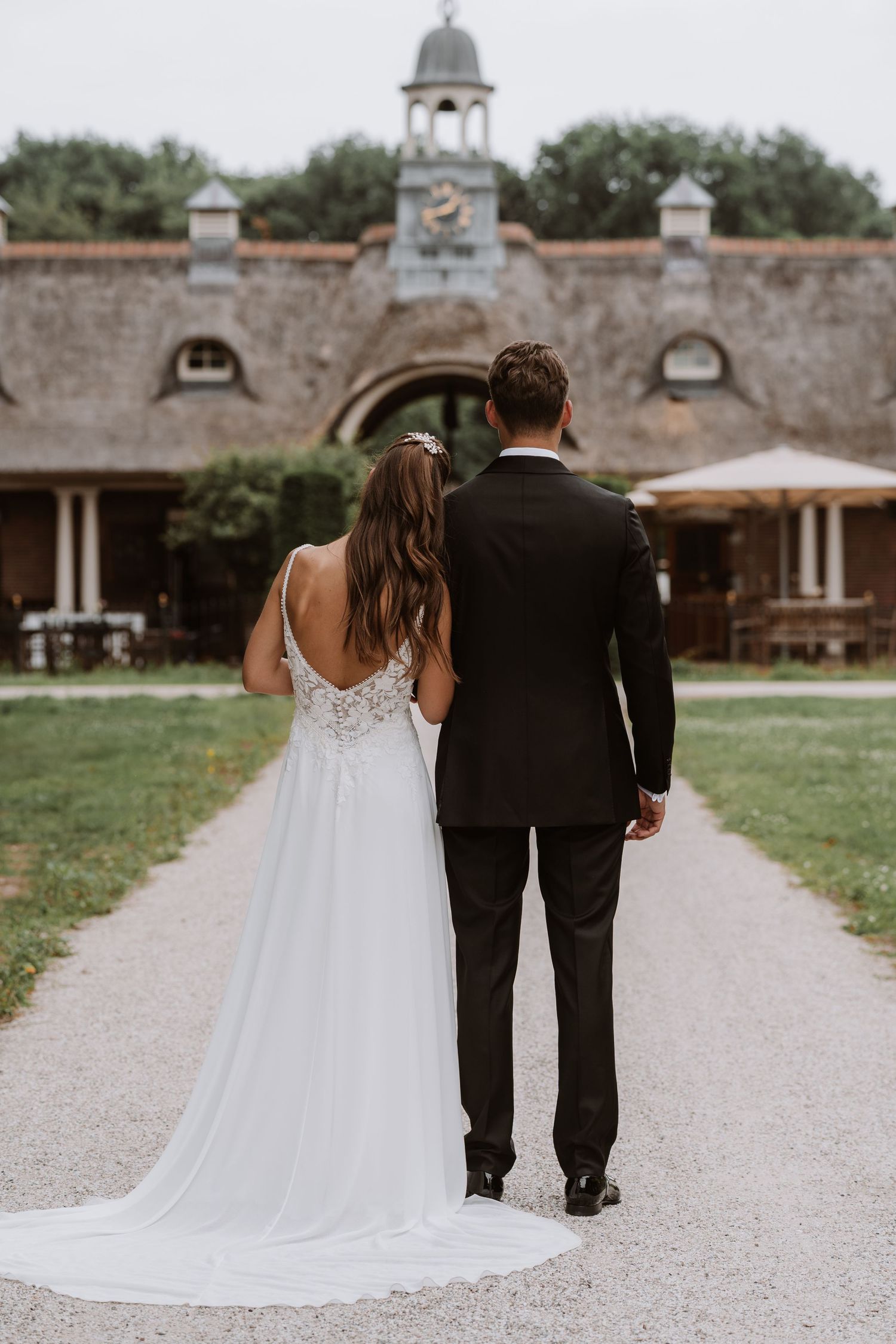 A wedding couple walks down a stone path with historic architecture in the background.