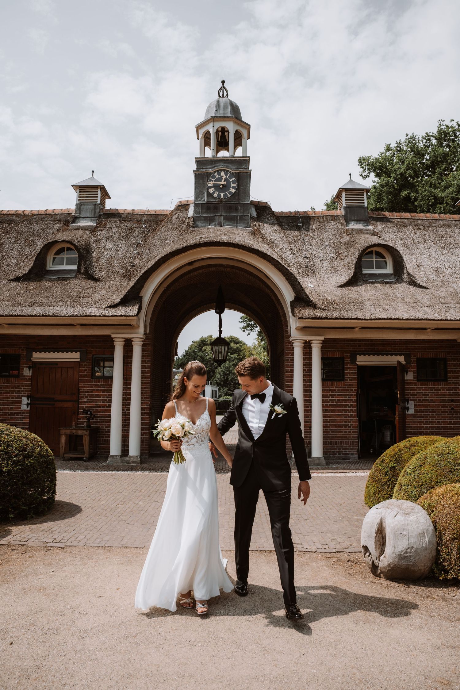 Wedding couple posing in front of a historic brick building with white columns and clock tower.